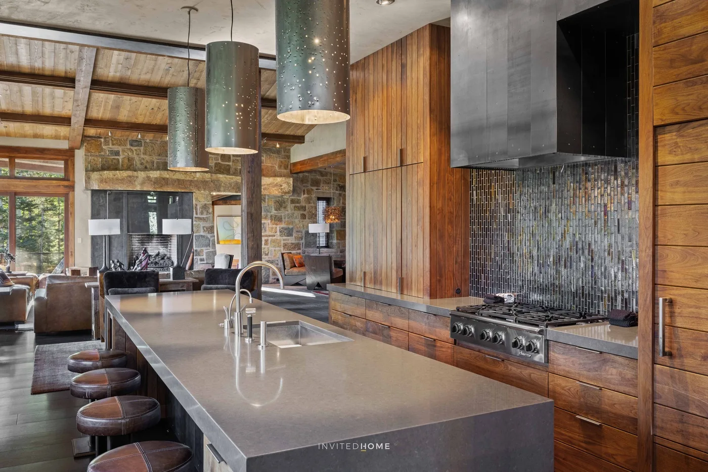 A kitchen with a long island and stools opens onto a living area.