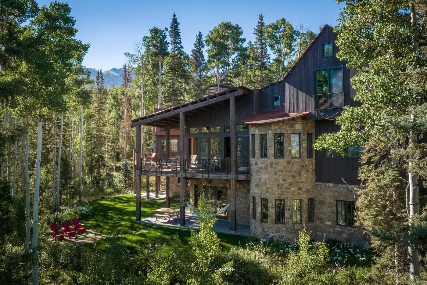 A multi-level house sits among trees, with a raised wooden deck and red outdoor chairs.