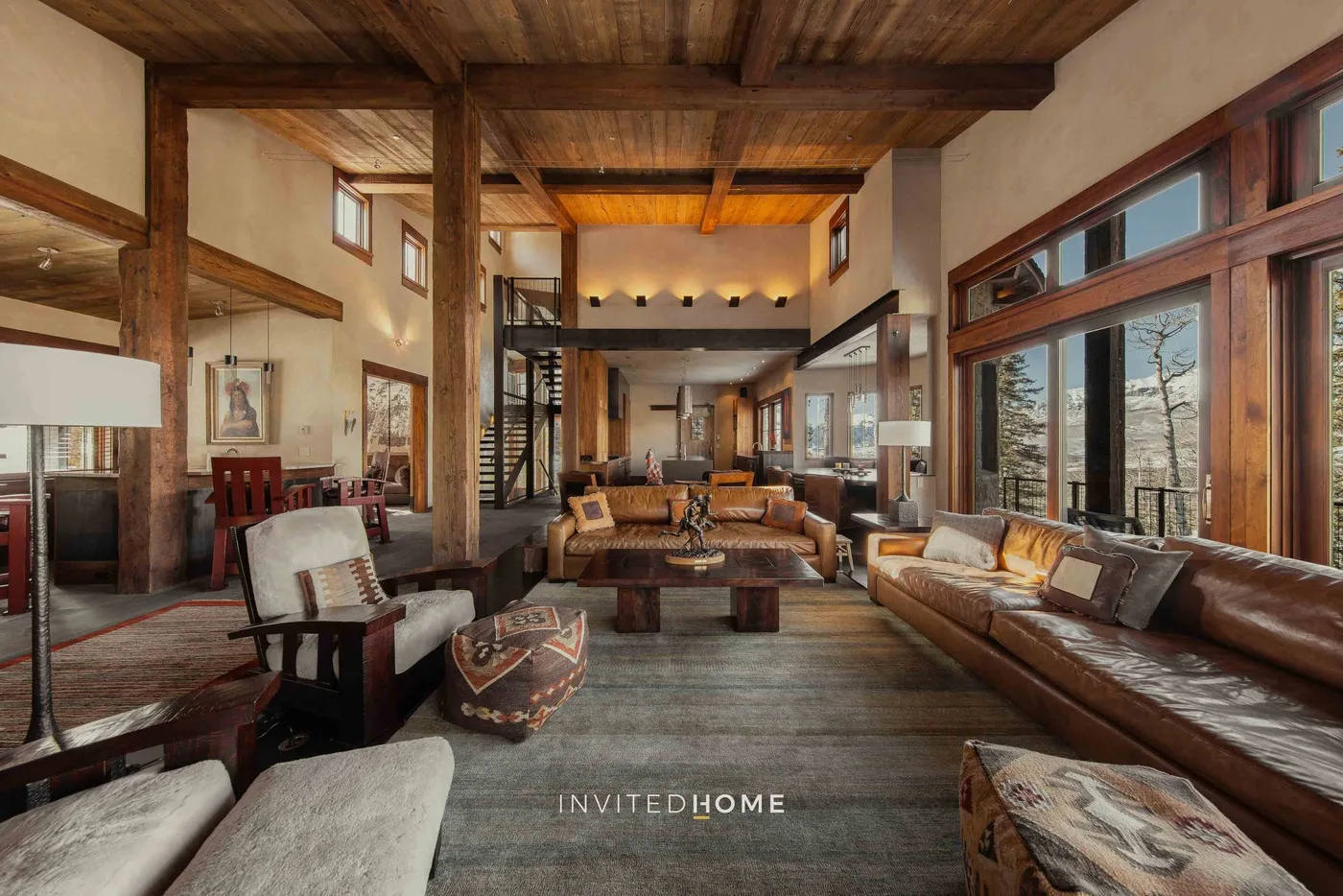 A spacious living room with wood beams, seating, and large windows.