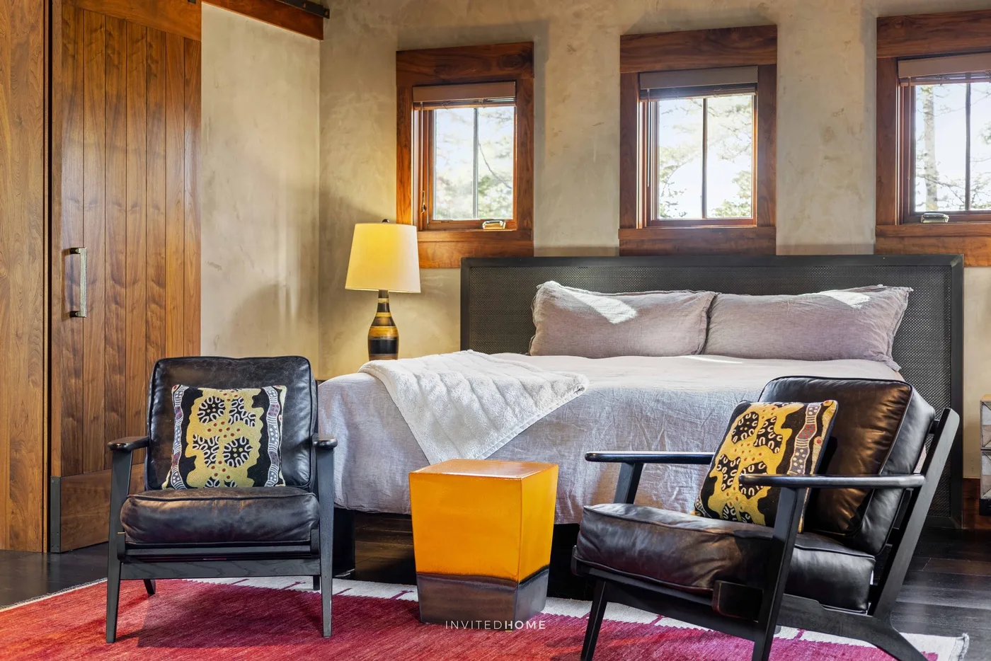 A bedroom with a bed, two armchairs, and windows along the wall.