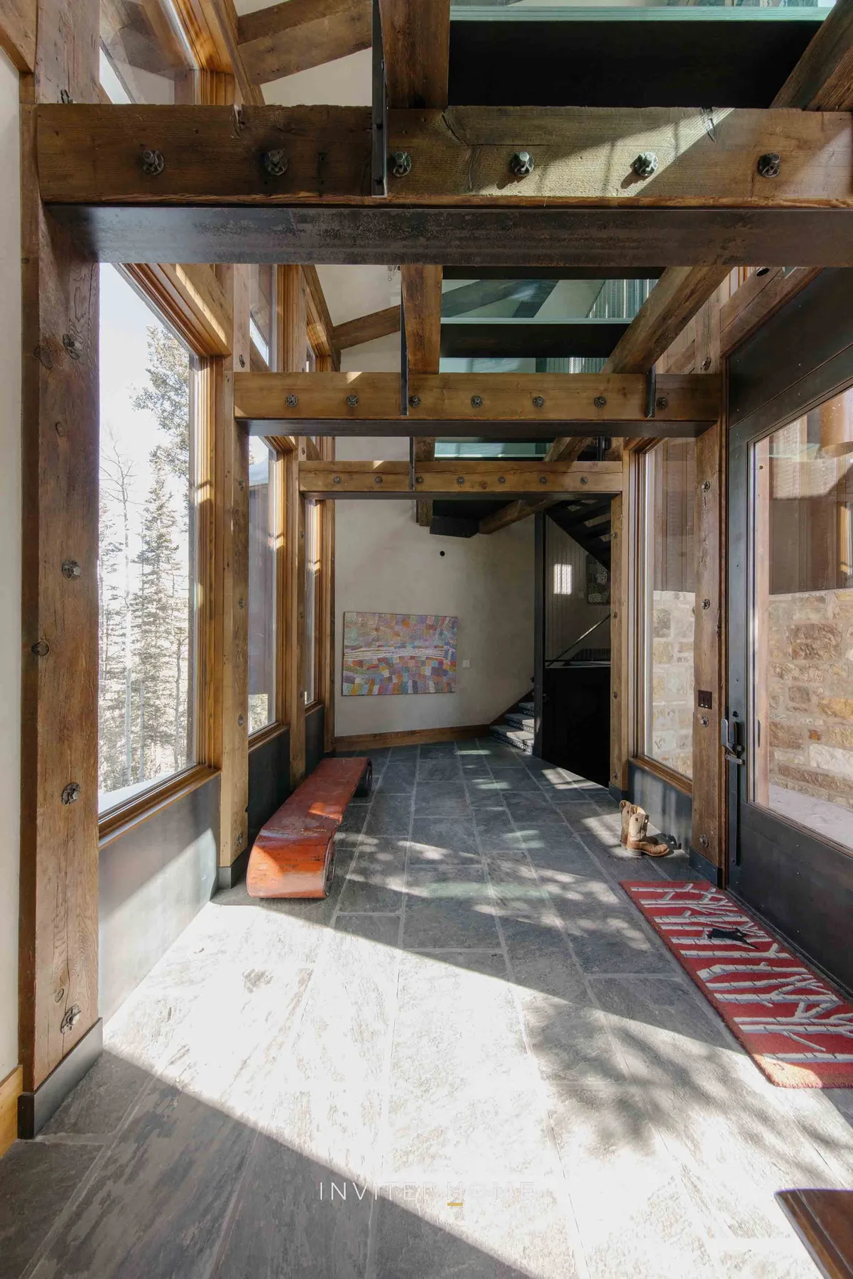 A sunlit glass hallway has exposed wooden beams and a tiled floor.