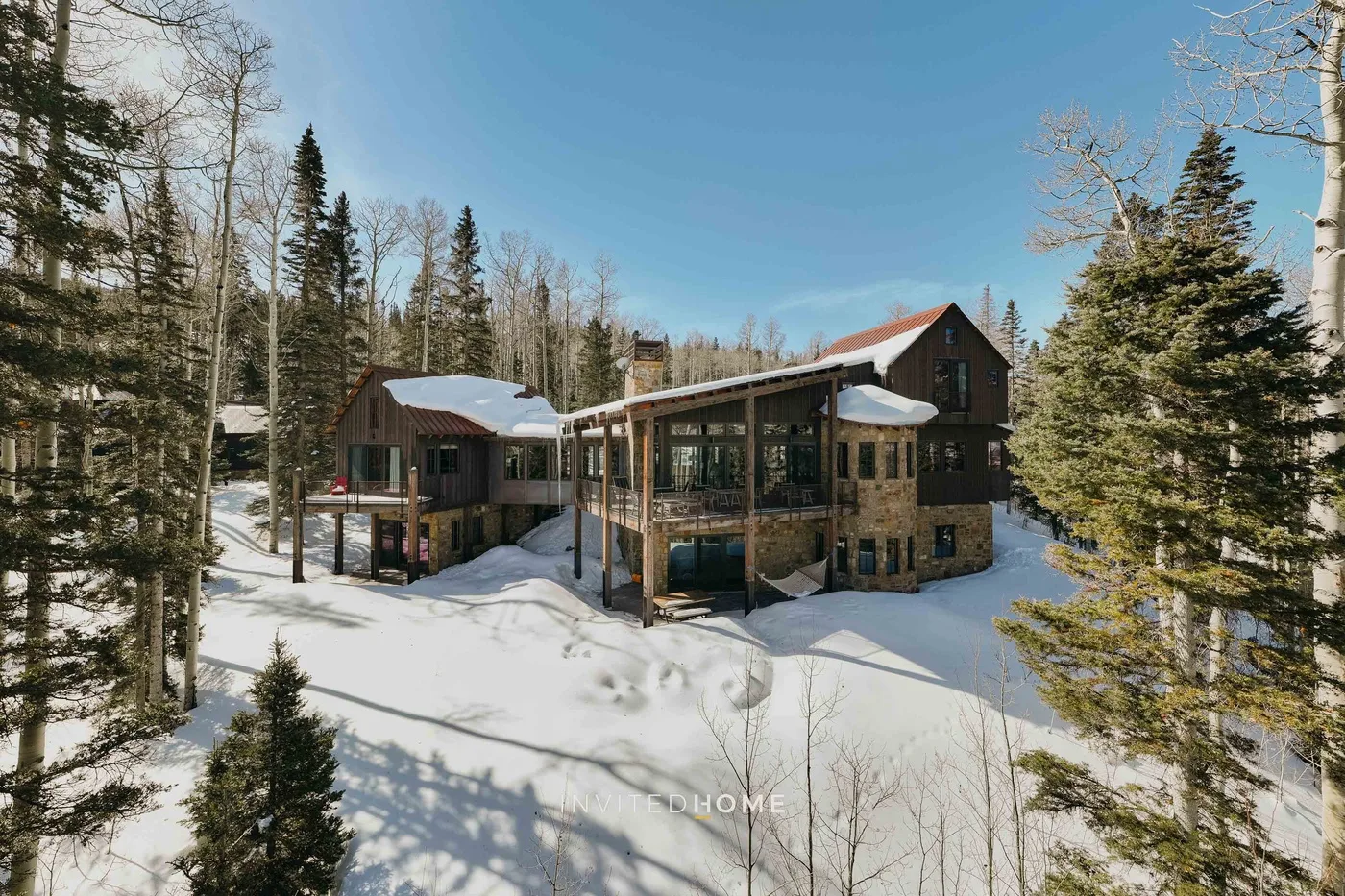 A large house stands among snow-covered trees beneath a clear blue sky.