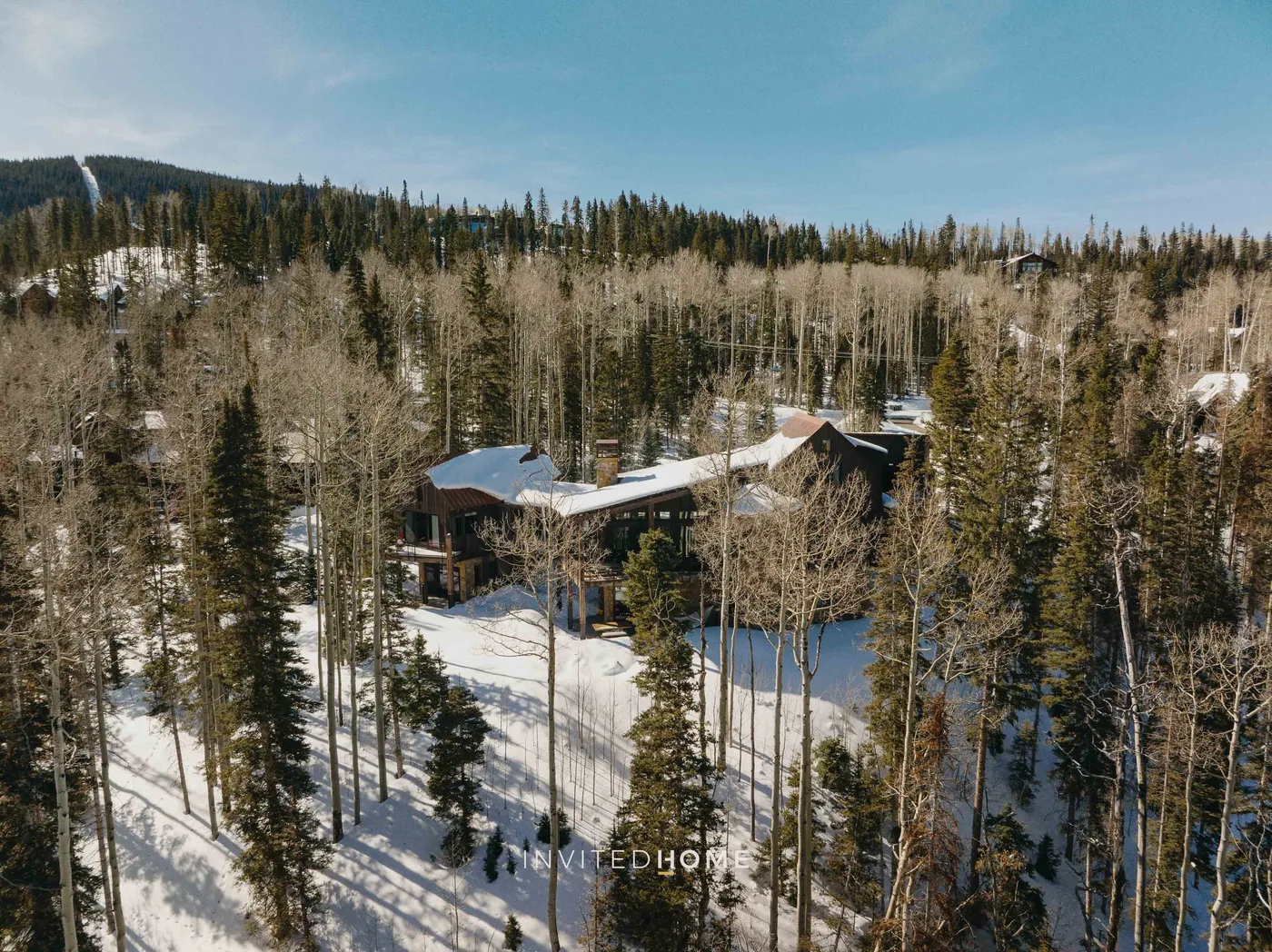 A lodge sits among snow-covered trees on a forested hillside.