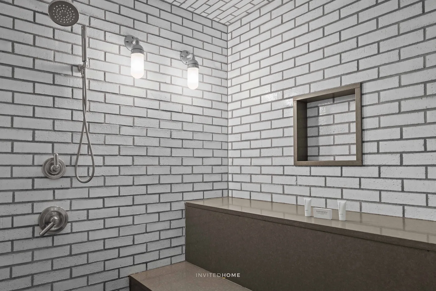 A tiled bathroom shower area with a wall niche and illuminated fixtures.