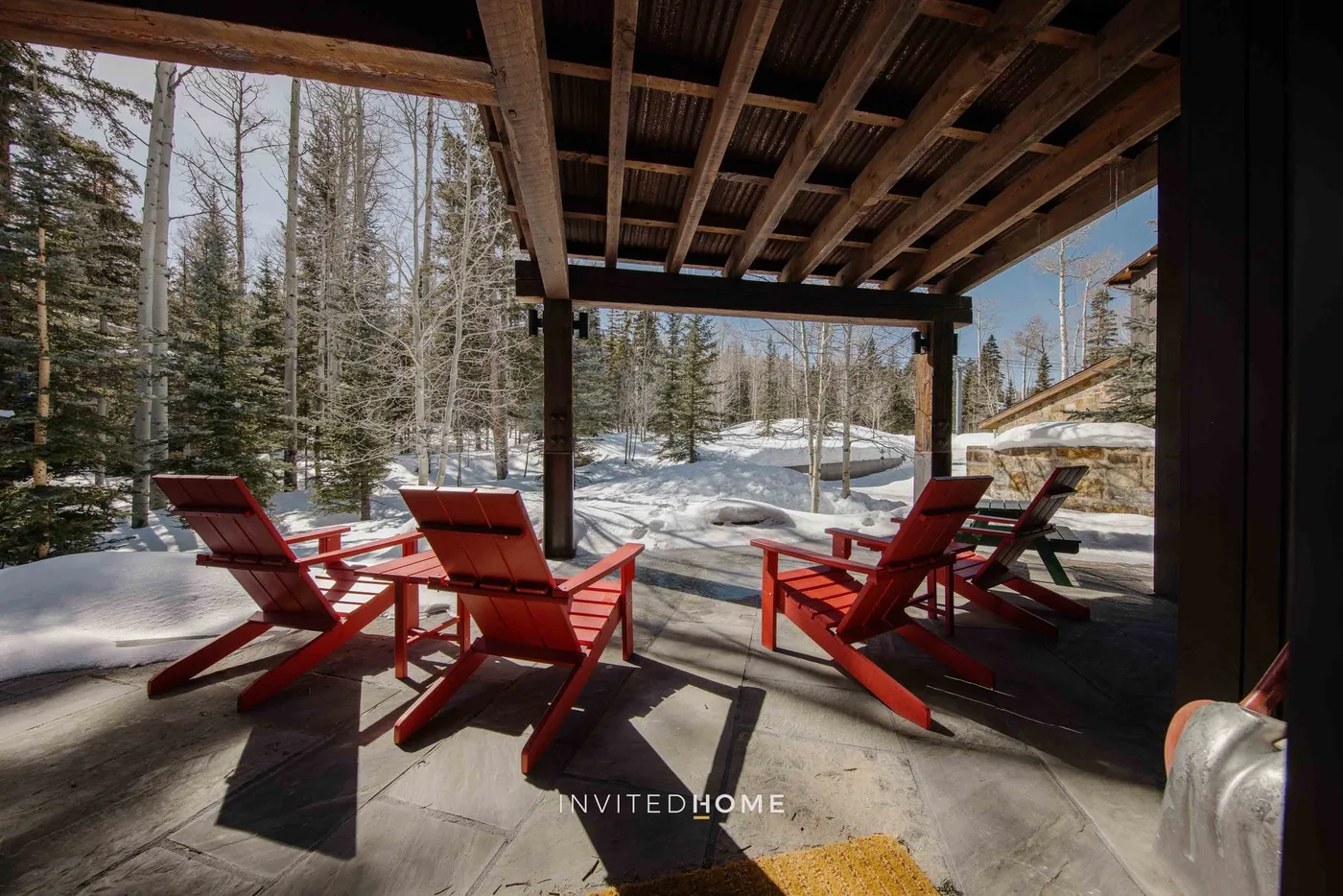 A covered outdoor patio with red seating overlooks a snowy wooded landscape.