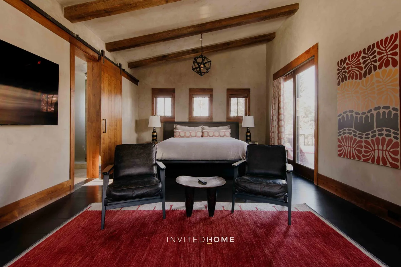 A bedroom with a bed, two armchairs, and a red rug.