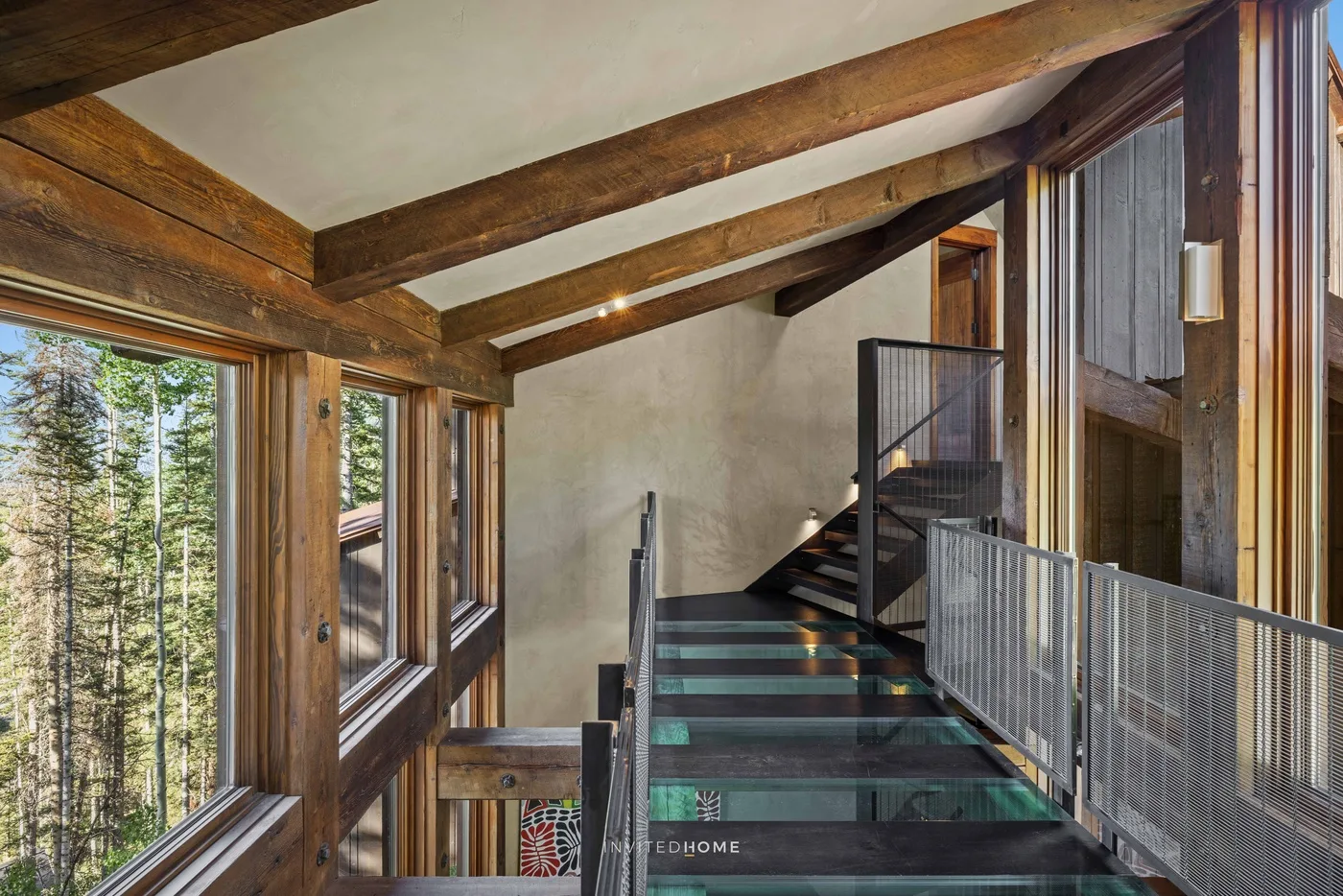 An interior staircase with dark steps and large windows overlooking trees.