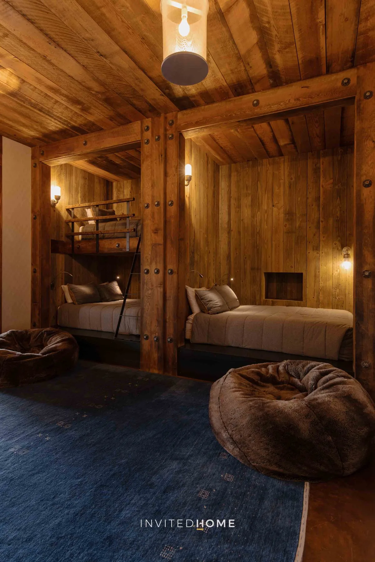 A wood-paneled bedroom with a bed, a lofted sleeping area, and floor cushions.