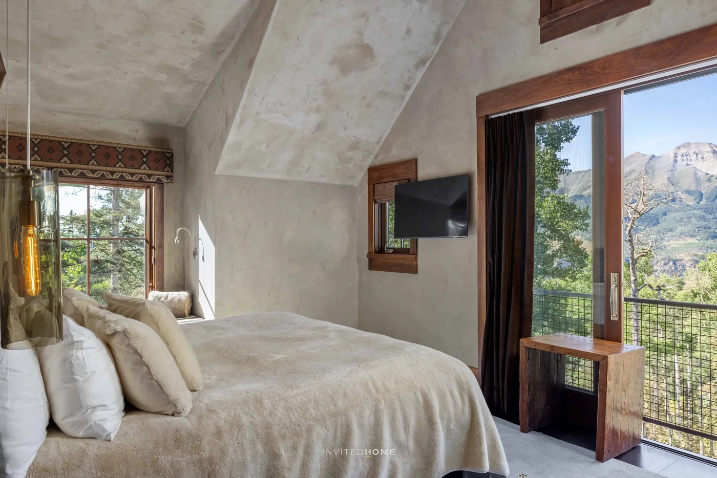 A bedroom with a large bed beside glass doors opening onto a mountain view.