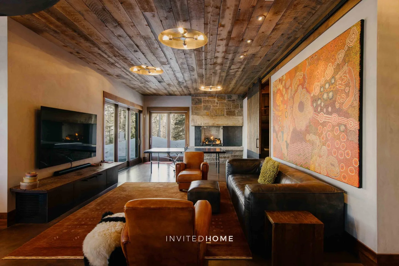 A rustic living room with seating, a fireplace, and a large colorful wall artwork.