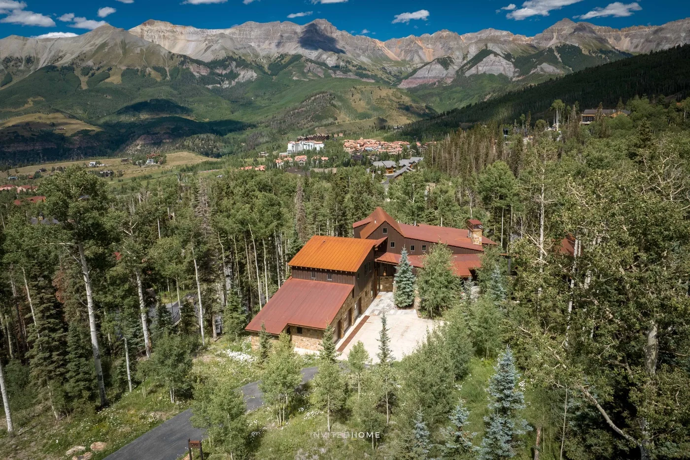 A mountain lodge sits among trees, with a valley and rugged peaks beyond.