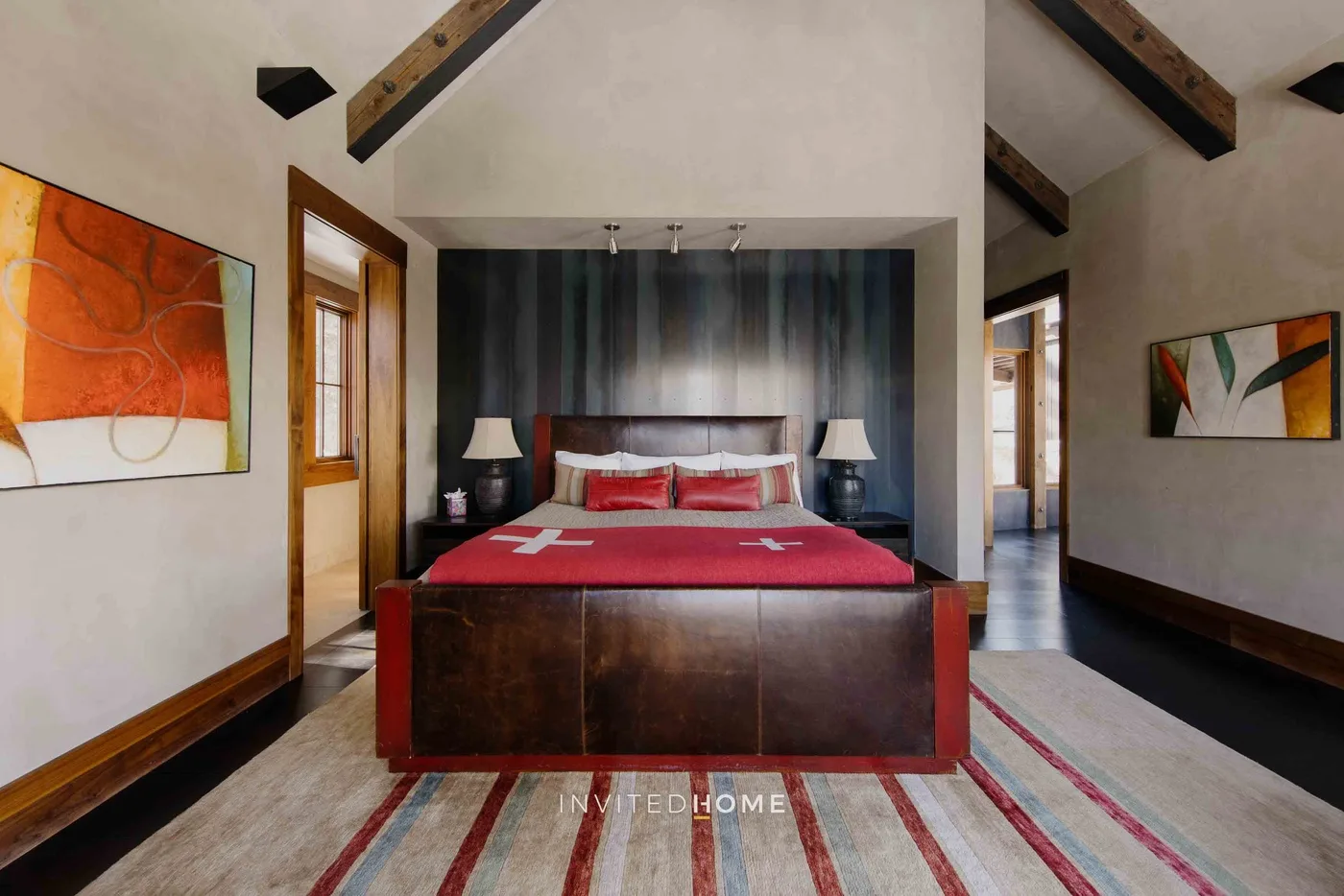 A bedroom with a bed, striped rug, and exposed ceiling beams.