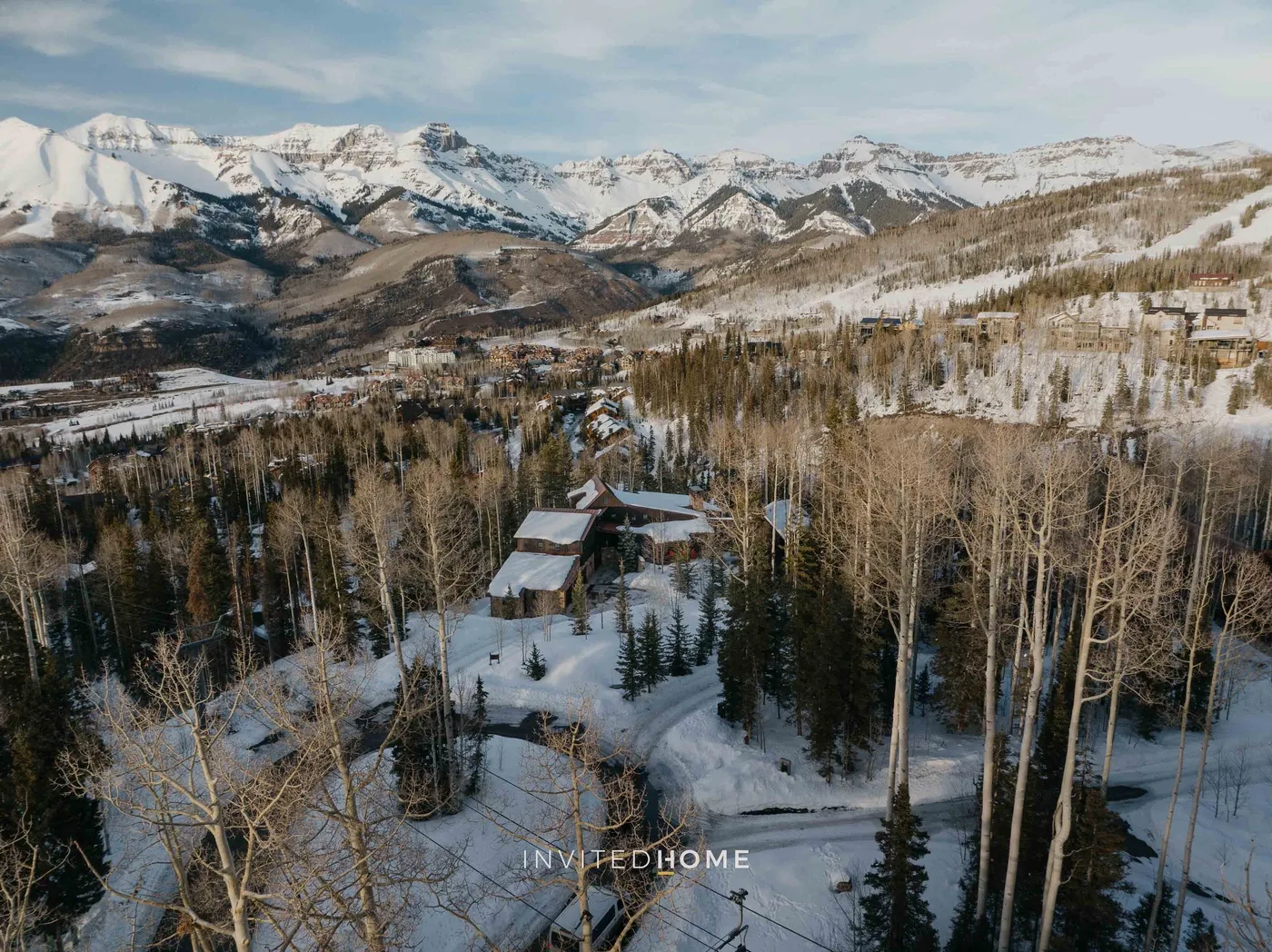 A snowy mountain landscape surrounds a wooded hillside with a cabin.