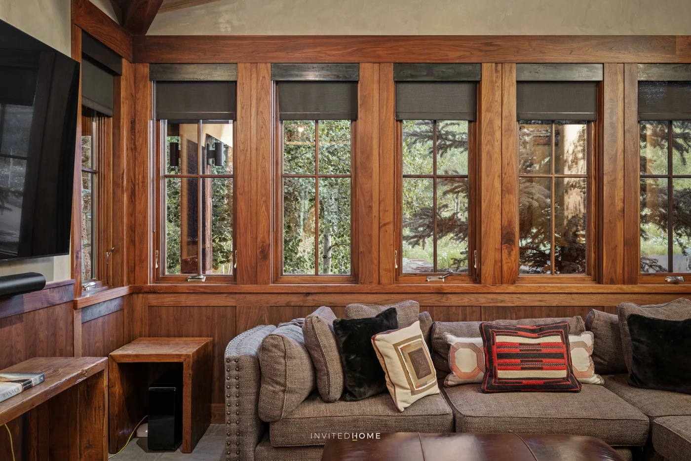 A wood-paneled living room with a sofa beneath a row of windows.