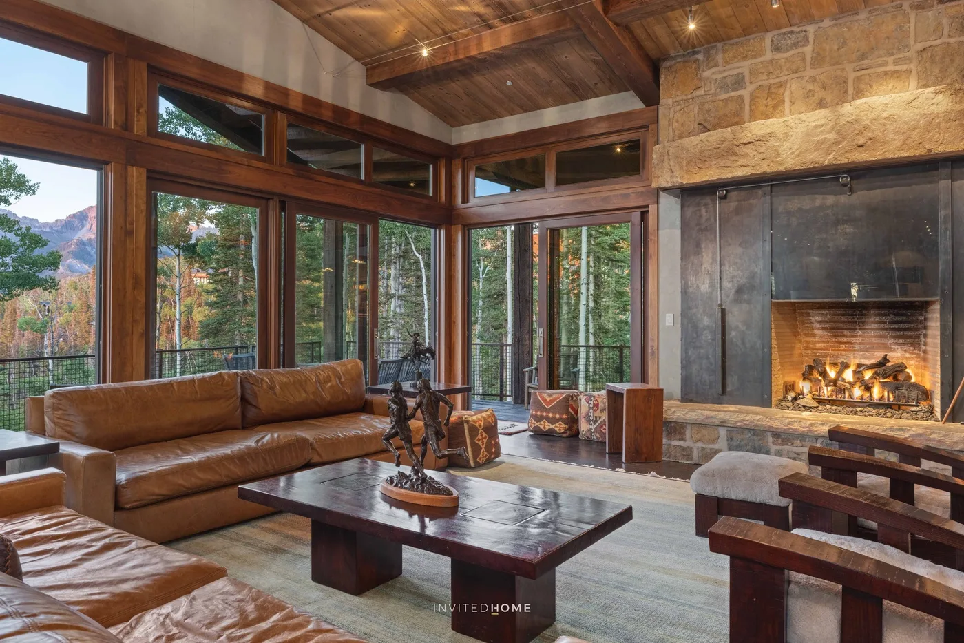 A living room with leather seating, large windows, and a stone fireplace.