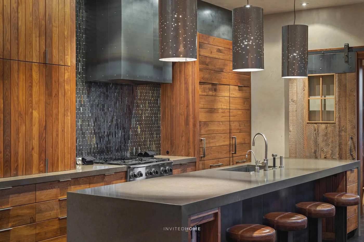 A modern kitchen with a large island, cooktop, and hanging pendant lights.