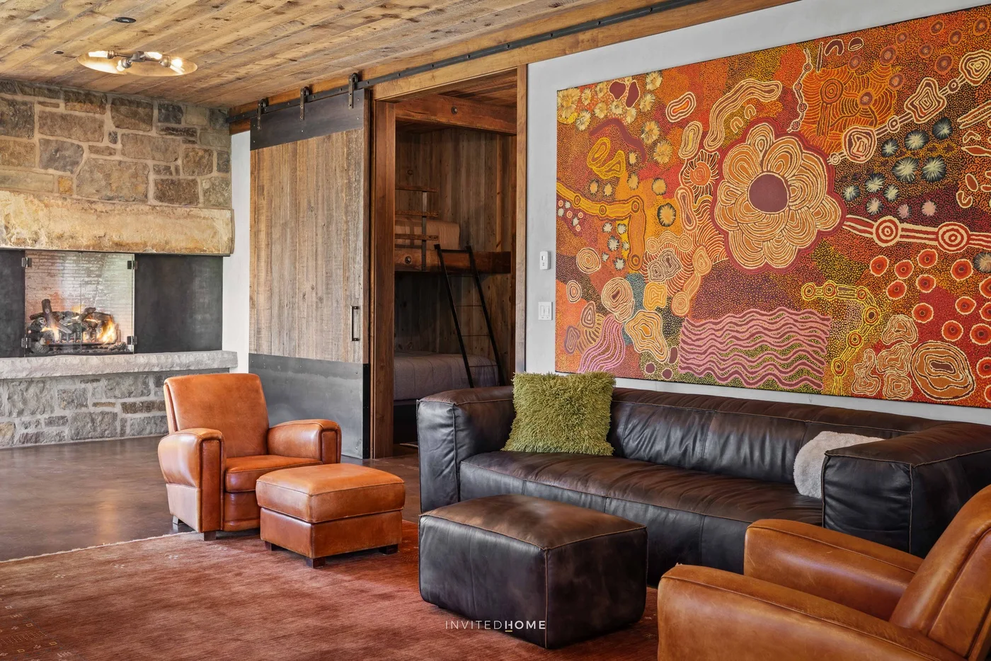 A living room with leather seating, a stone fireplace, and colorful wall art.