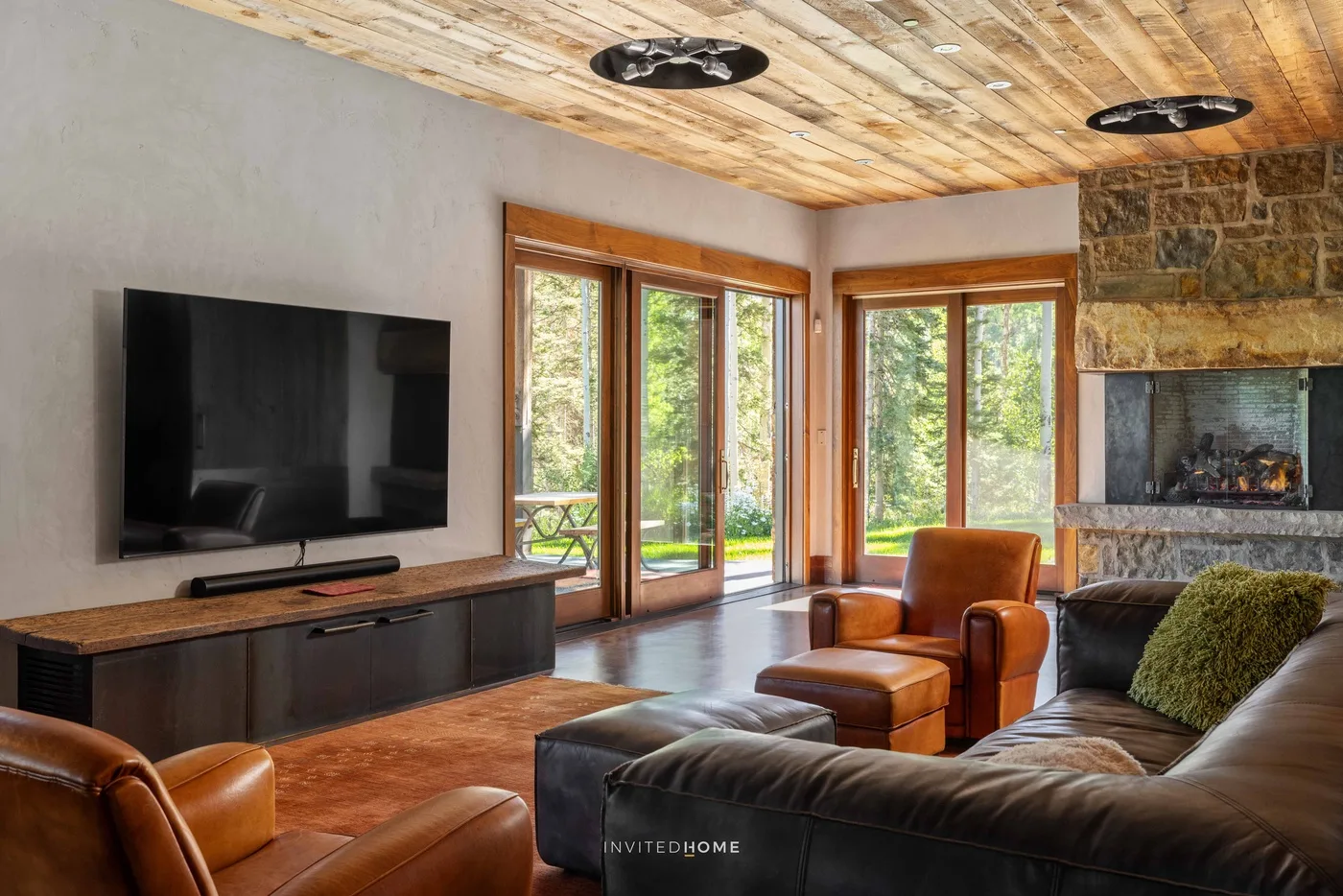 A living room with seating, a television, and large windows overlooking greenery.