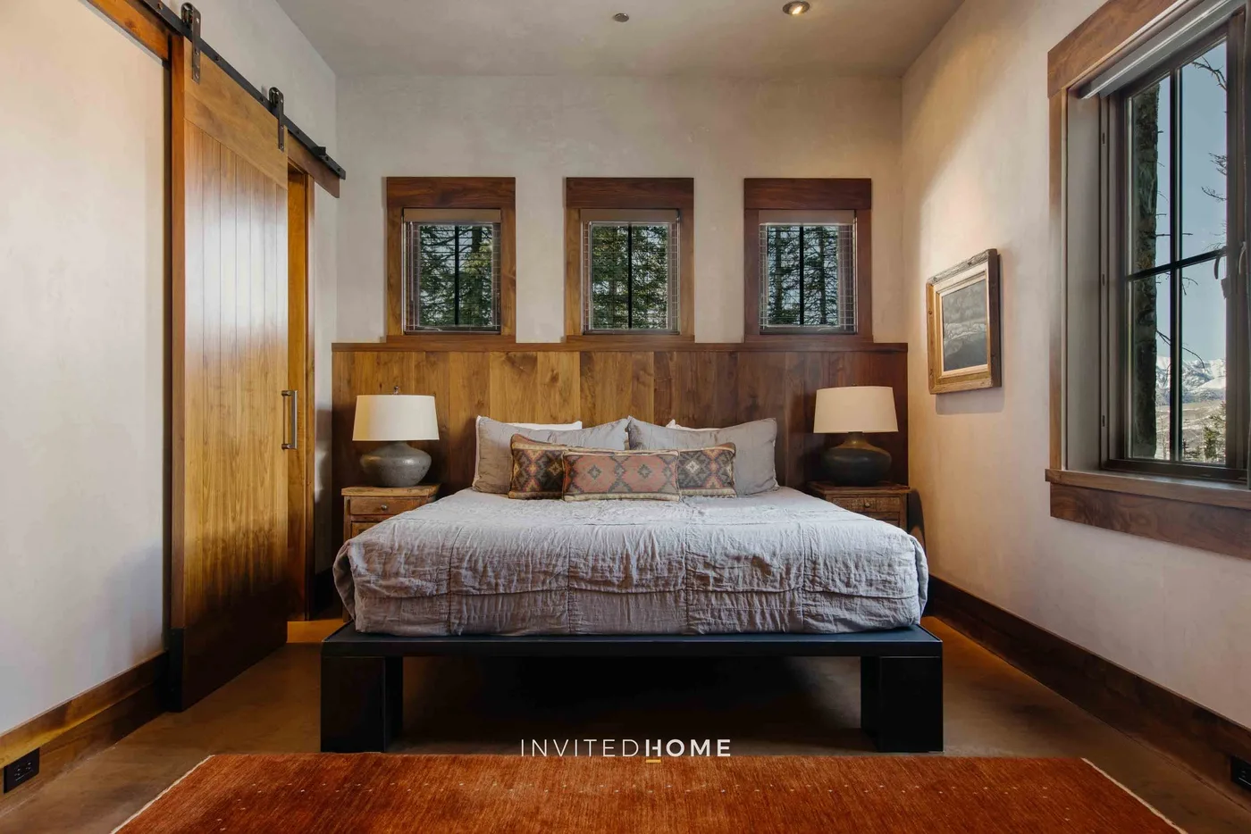 A bedroom with a bed beneath three small windows and a large side window.