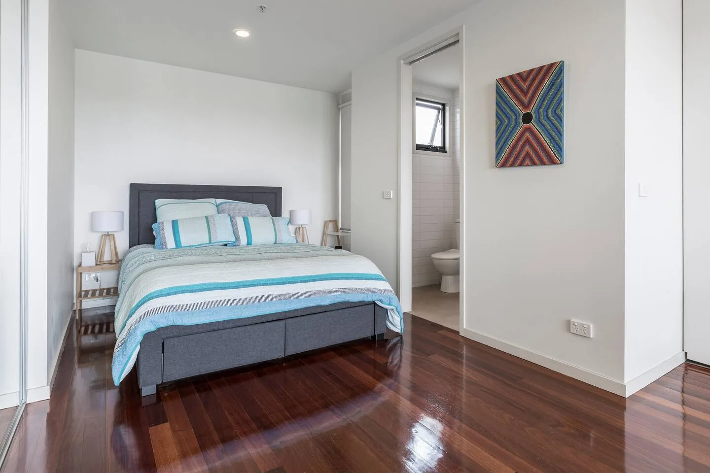 Un dormitorio con una cama vestida con ropa de cama azul y blanca y mesas de noche.