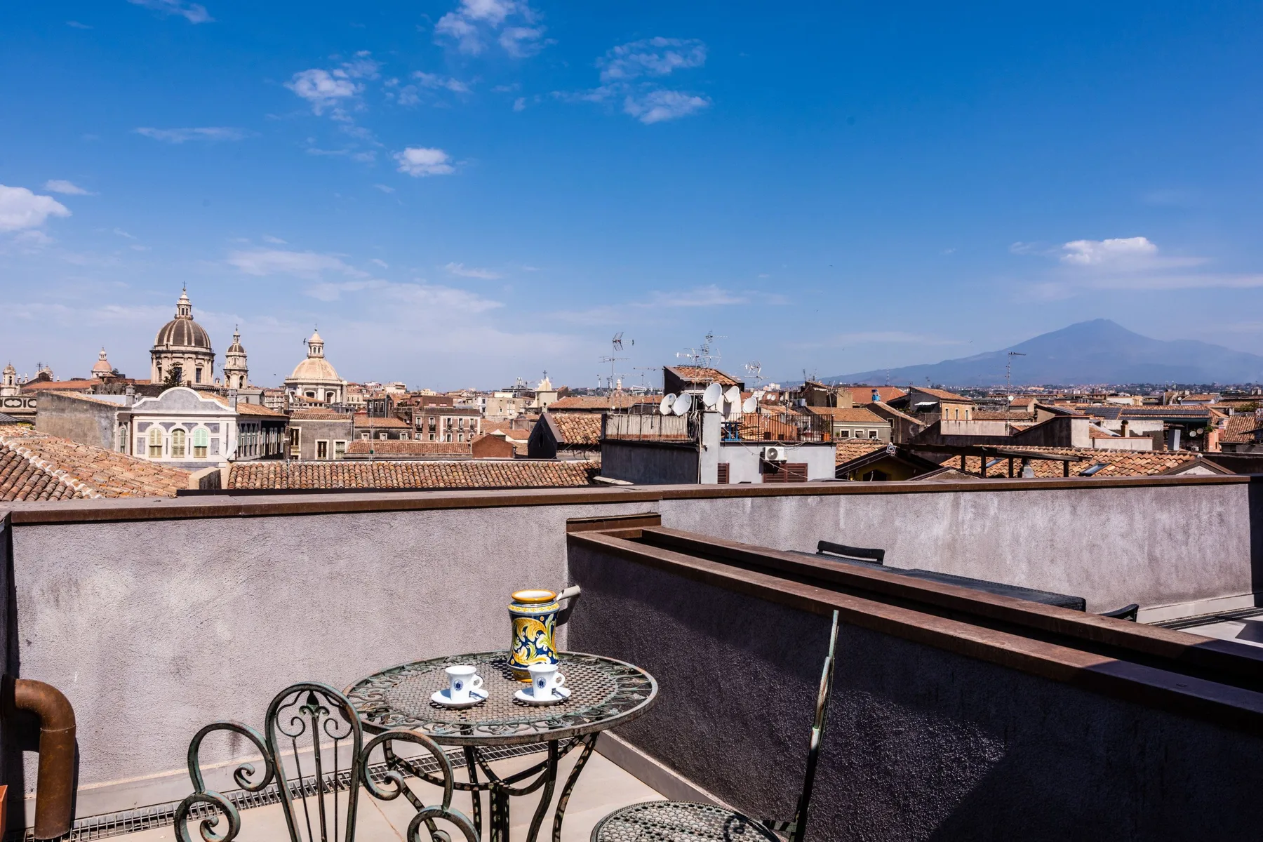 A rooftop terrace overlooks a historic city skyline beneath a clear blue sky.