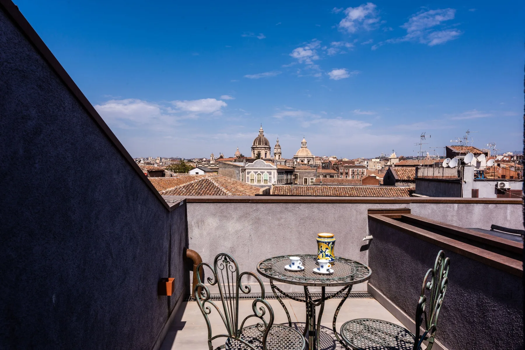A rooftop terrace with a small metal table overlooking a city skyline.