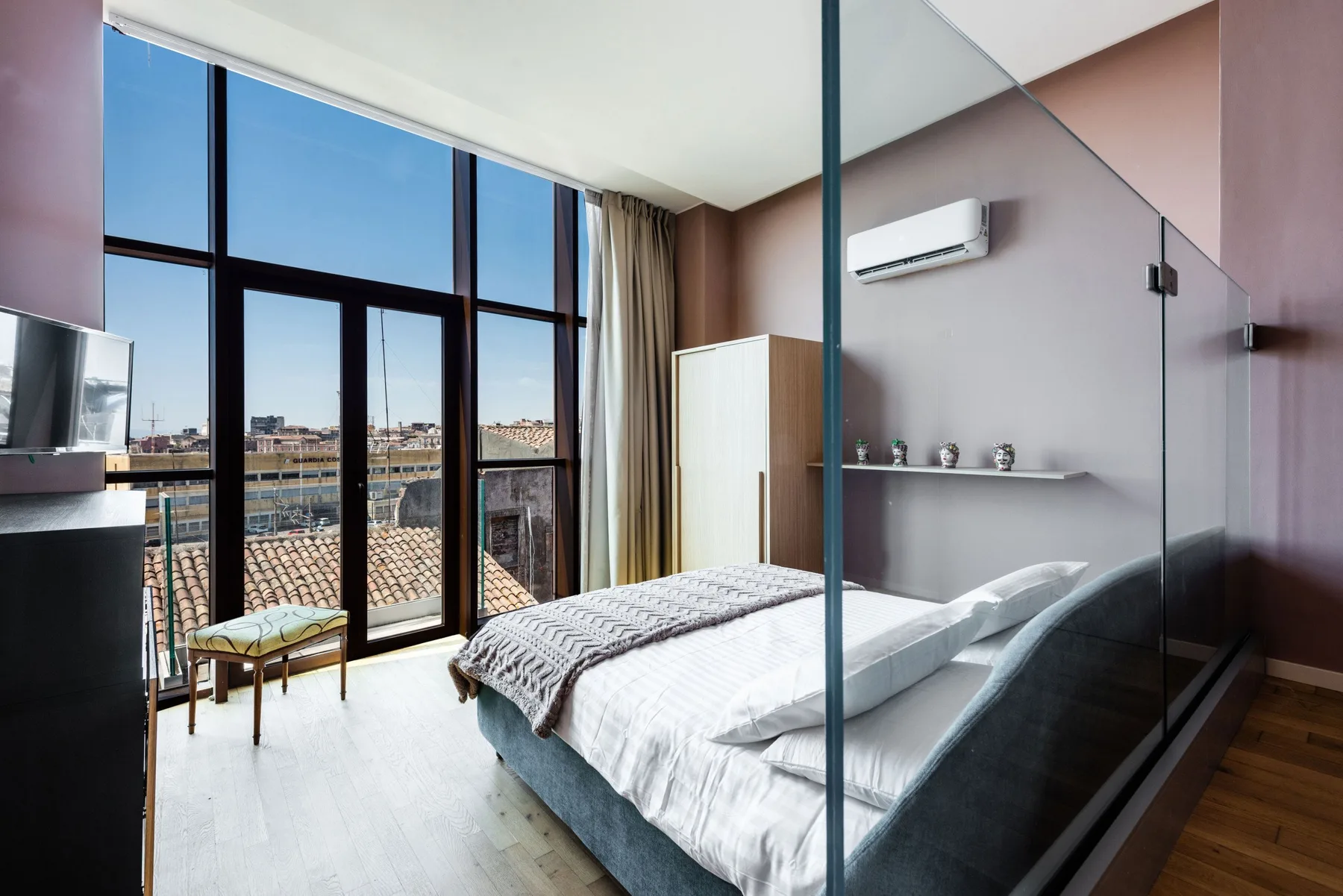 A bedroom with a bed beside tall windows and a glass partition.