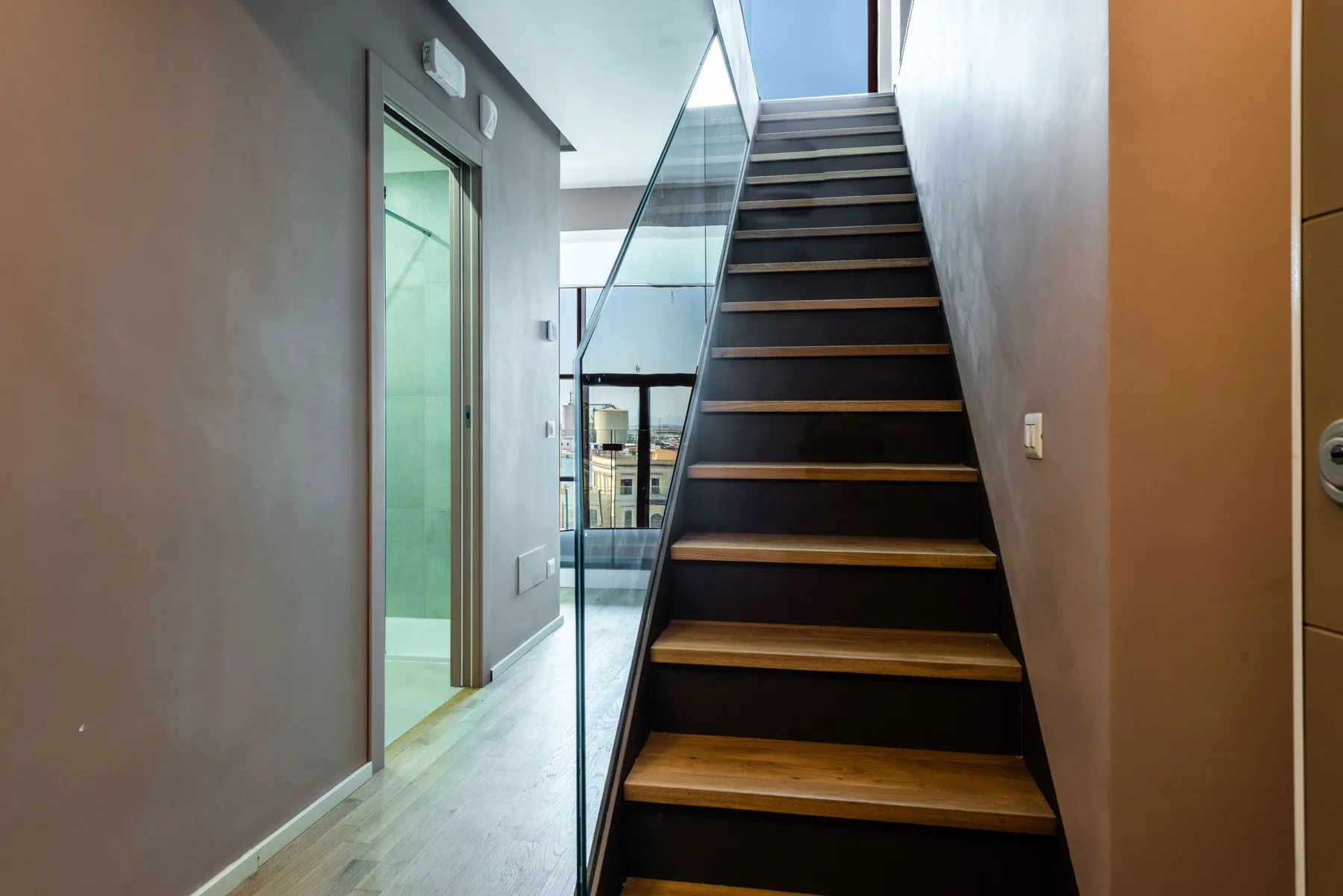 An interior staircase with dark steps and a glass railing.