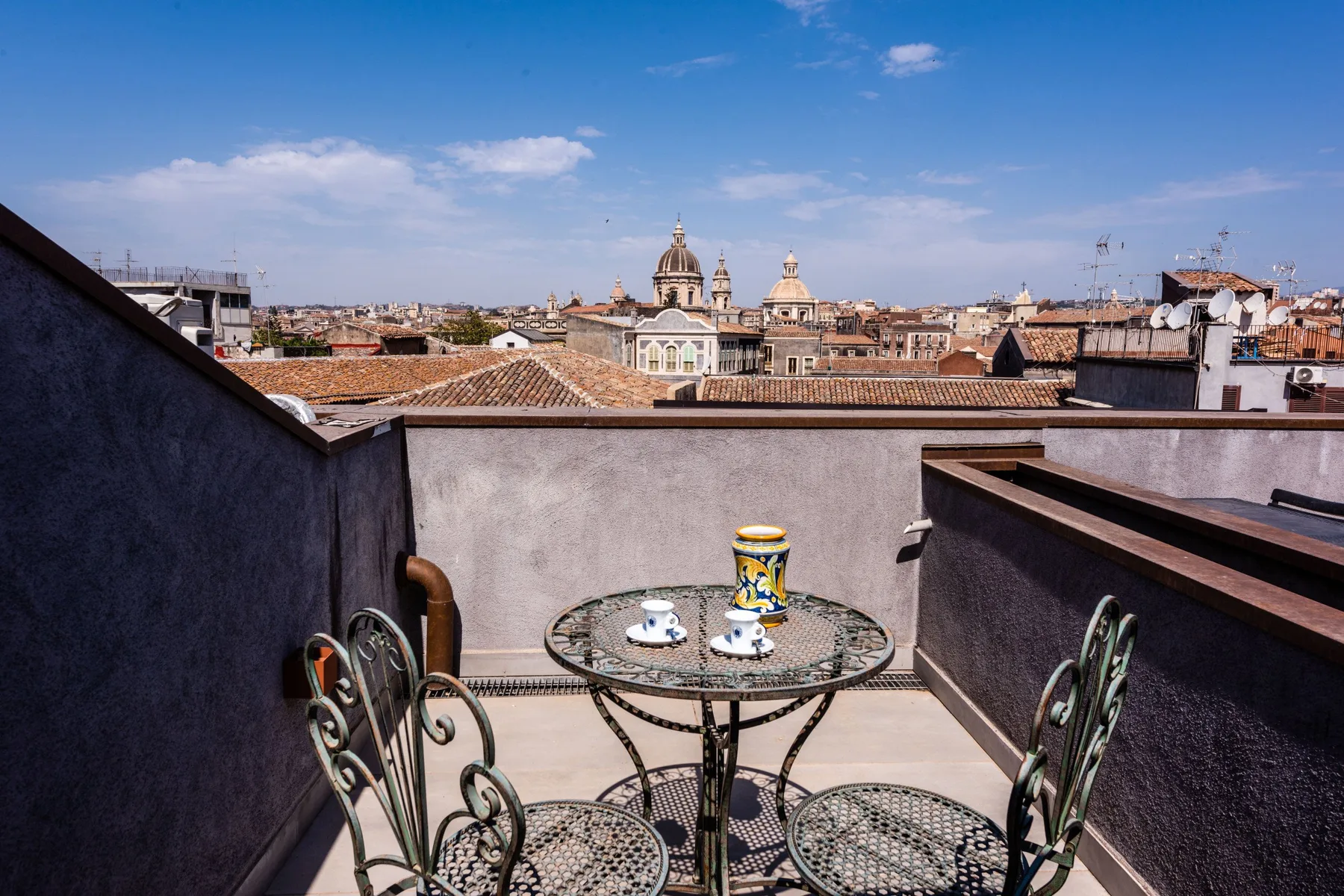 A rooftop terrace with a small table and chairs overlooks a city skyline.