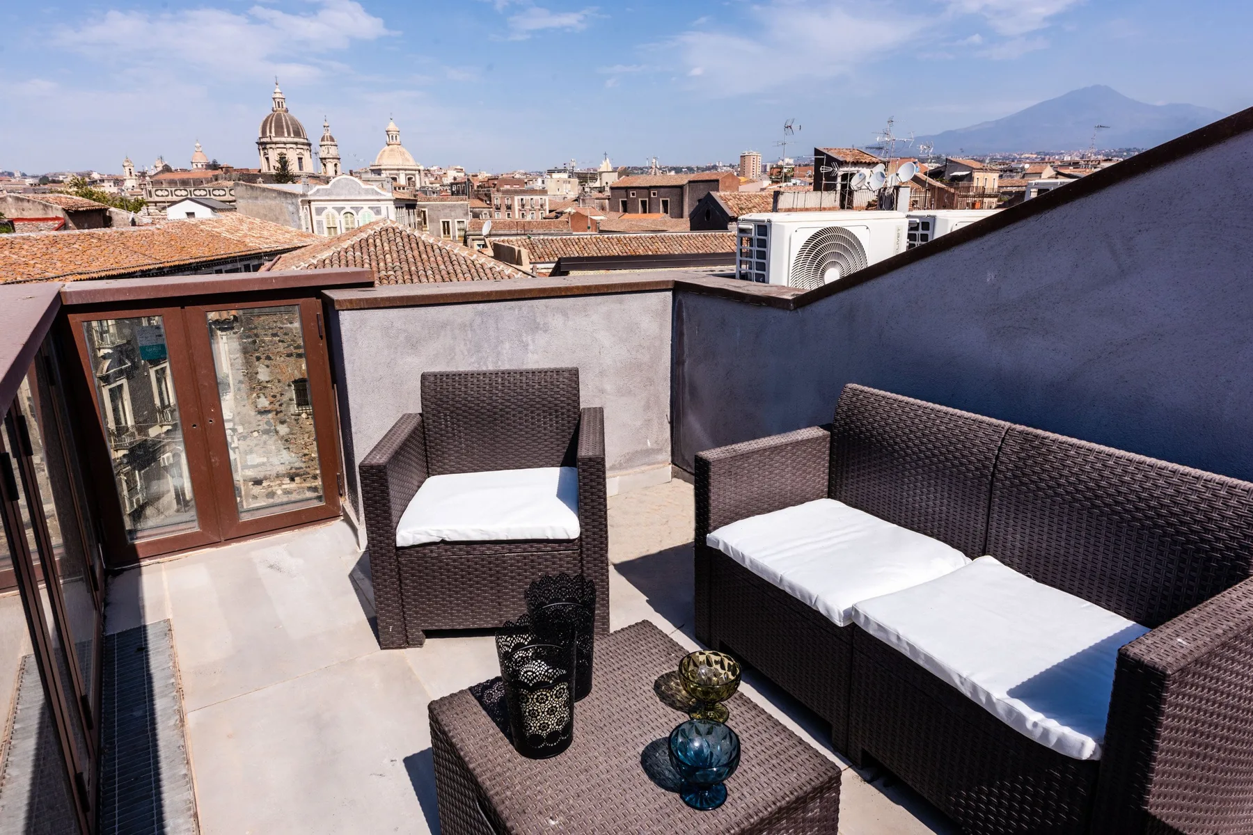 A rooftop terrace with dark wicker seating overlooks the surrounding city.