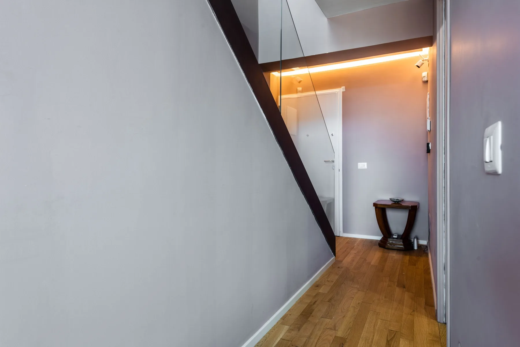 A narrow hallway with wood flooring and a small table at the end.