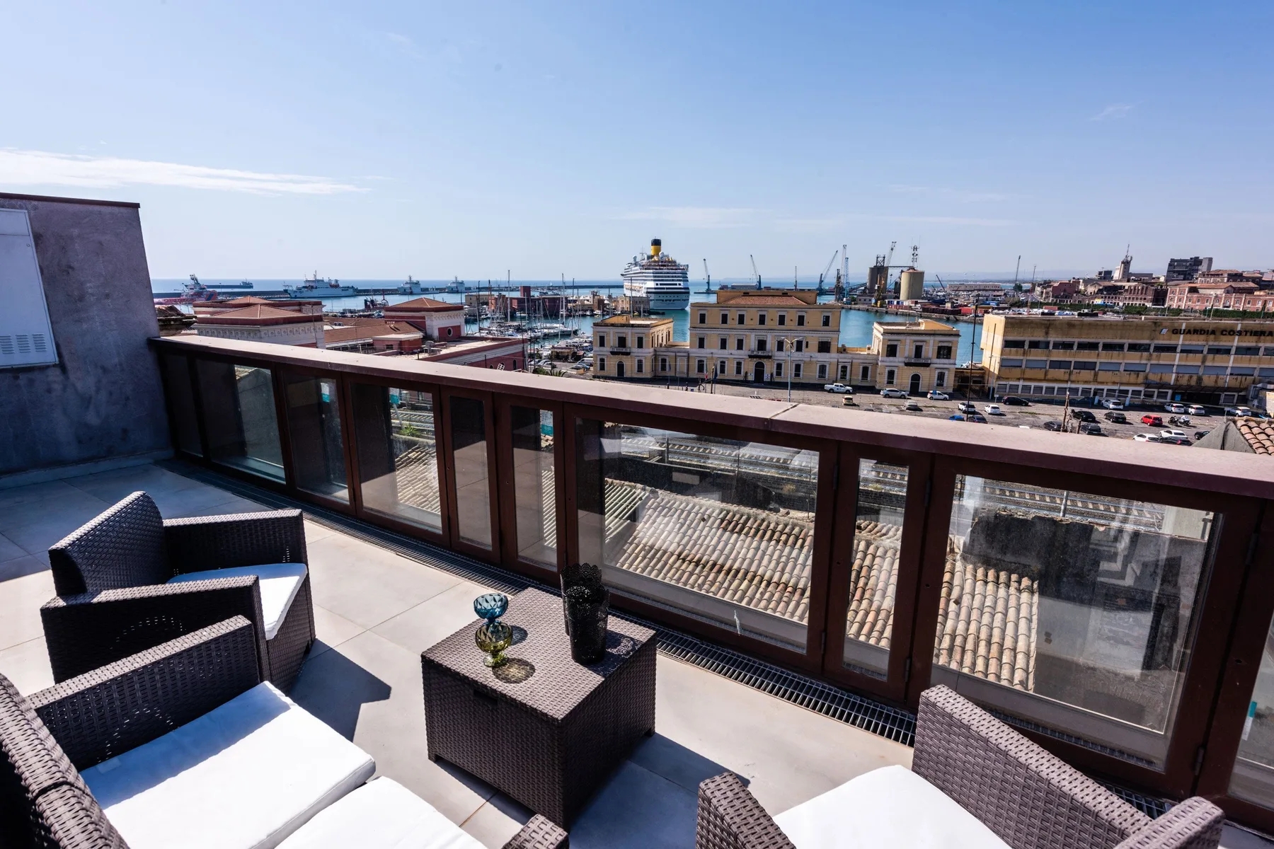 A rooftop terrace with outdoor seating overlooks a harbor and surrounding city.