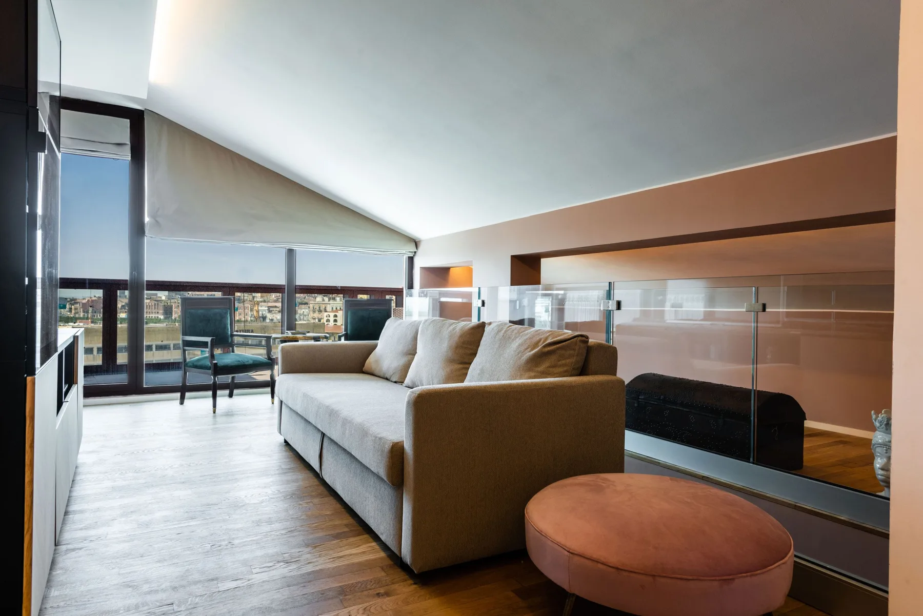 A modern living room with a sofa beside a glass railing and large windows.