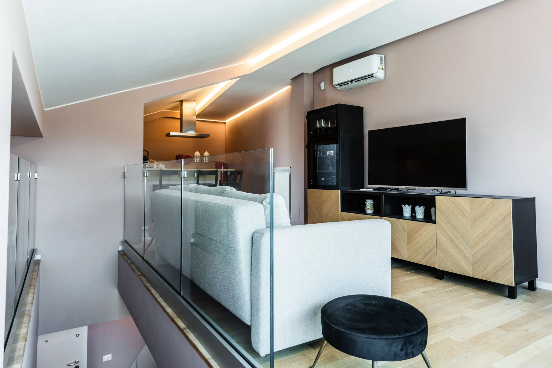 A modern living area with light seating, a television, and glass railing.