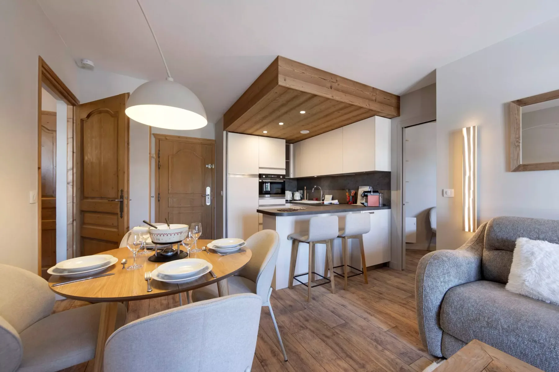 Zona de comedor y cocina con una mesa de madera y una pequeña barra.