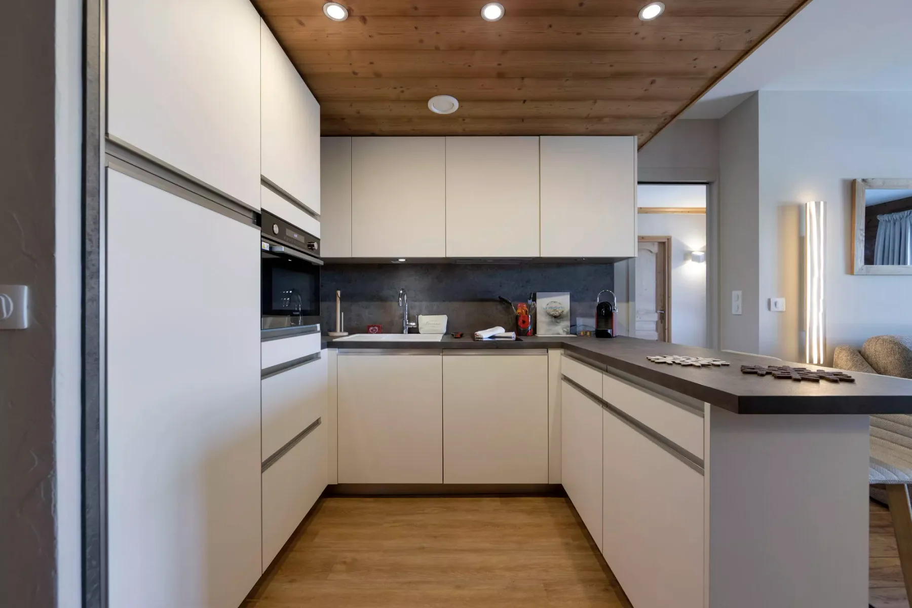 Una cocina moderna con gabinetes claros, encimeras oscuras y techo de madera.
