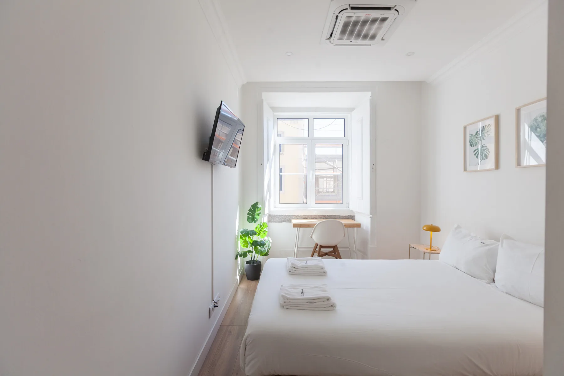 A bright bedroom with a bed, window, and small desk.