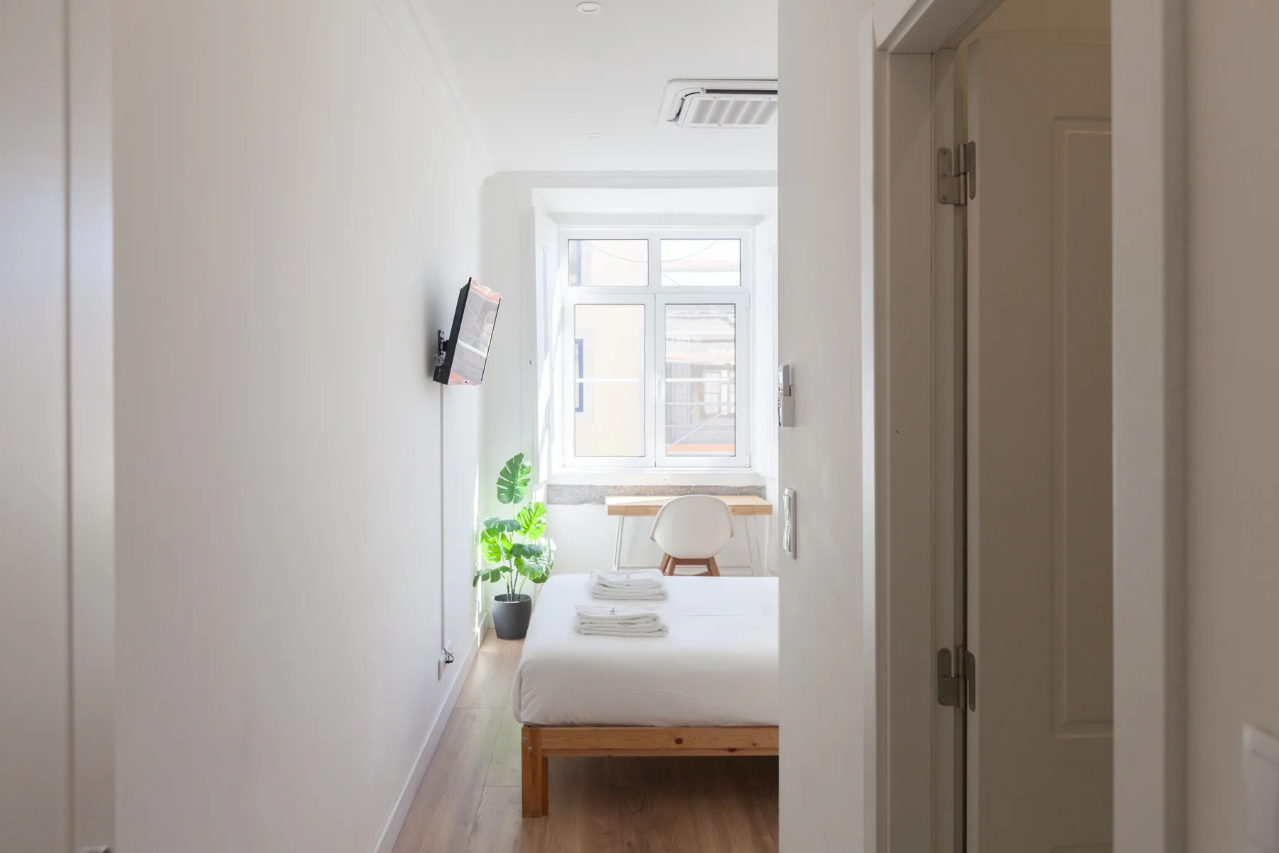 A bright bedroom with a bed, a desk, and a window at the far end.