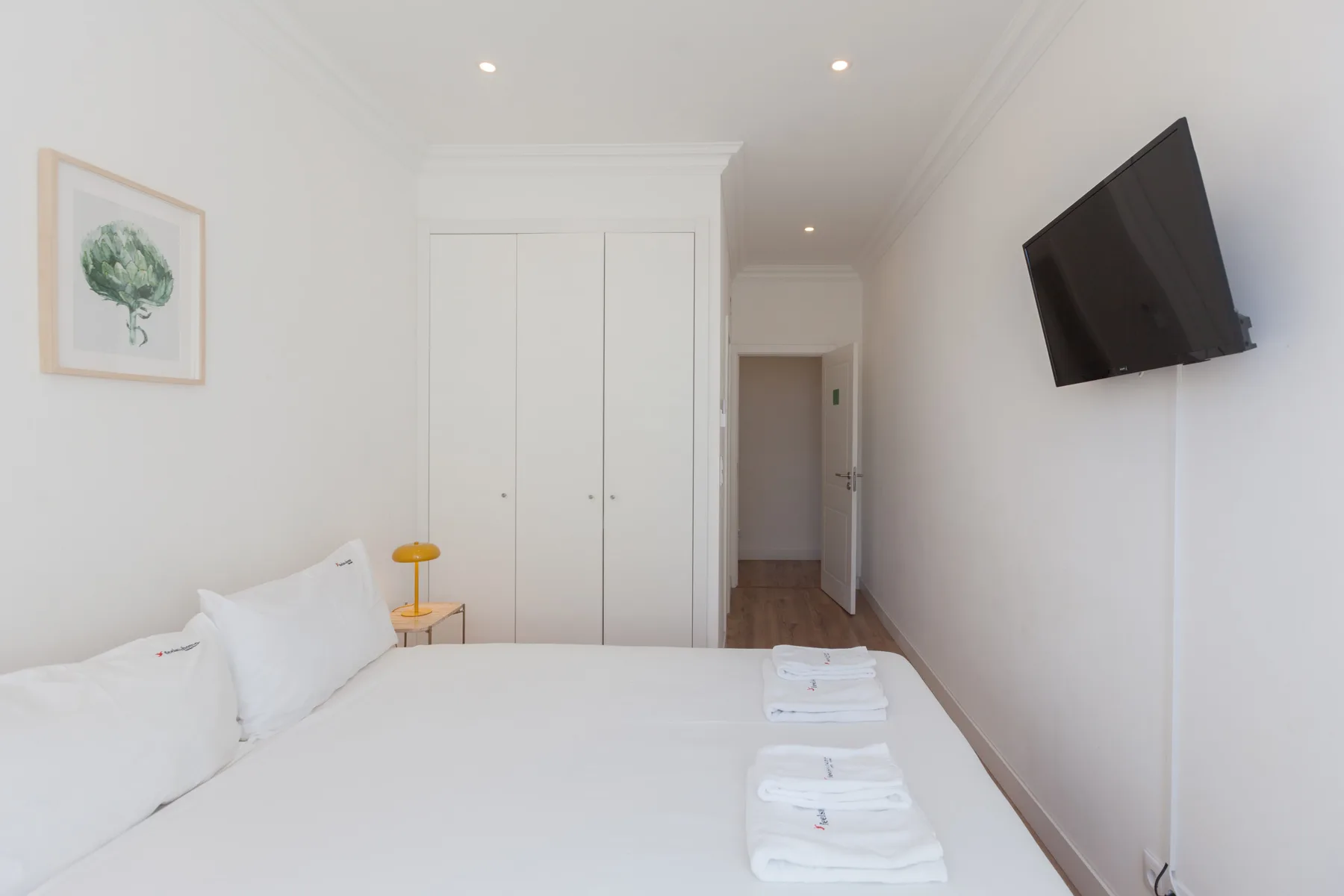 A bright bedroom with a neatly made bed and a wall-mounted television.