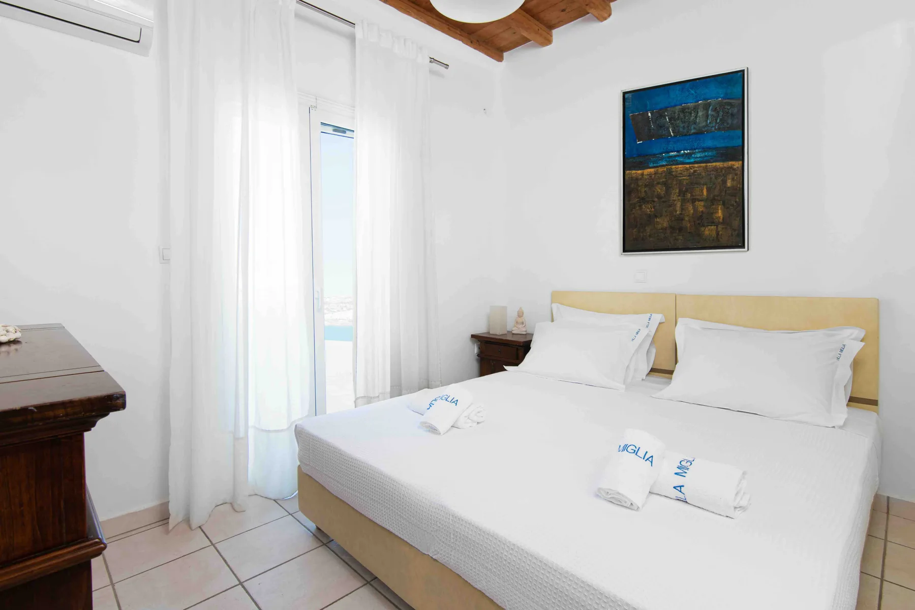 A bright bedroom with a bed, white linens, and sheer curtains.