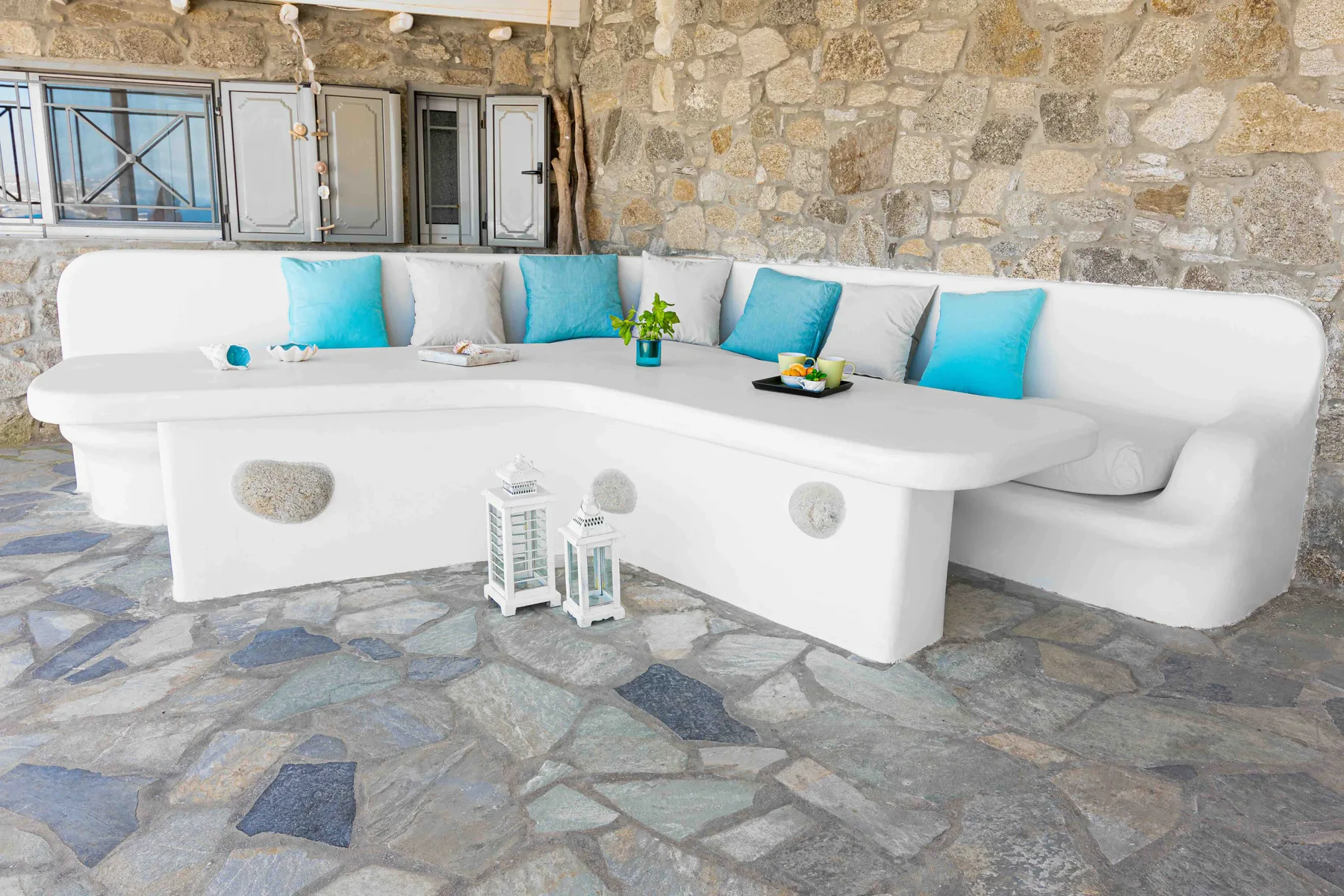 A white built-in seating area with turquoise cushions sits against a stone wall.