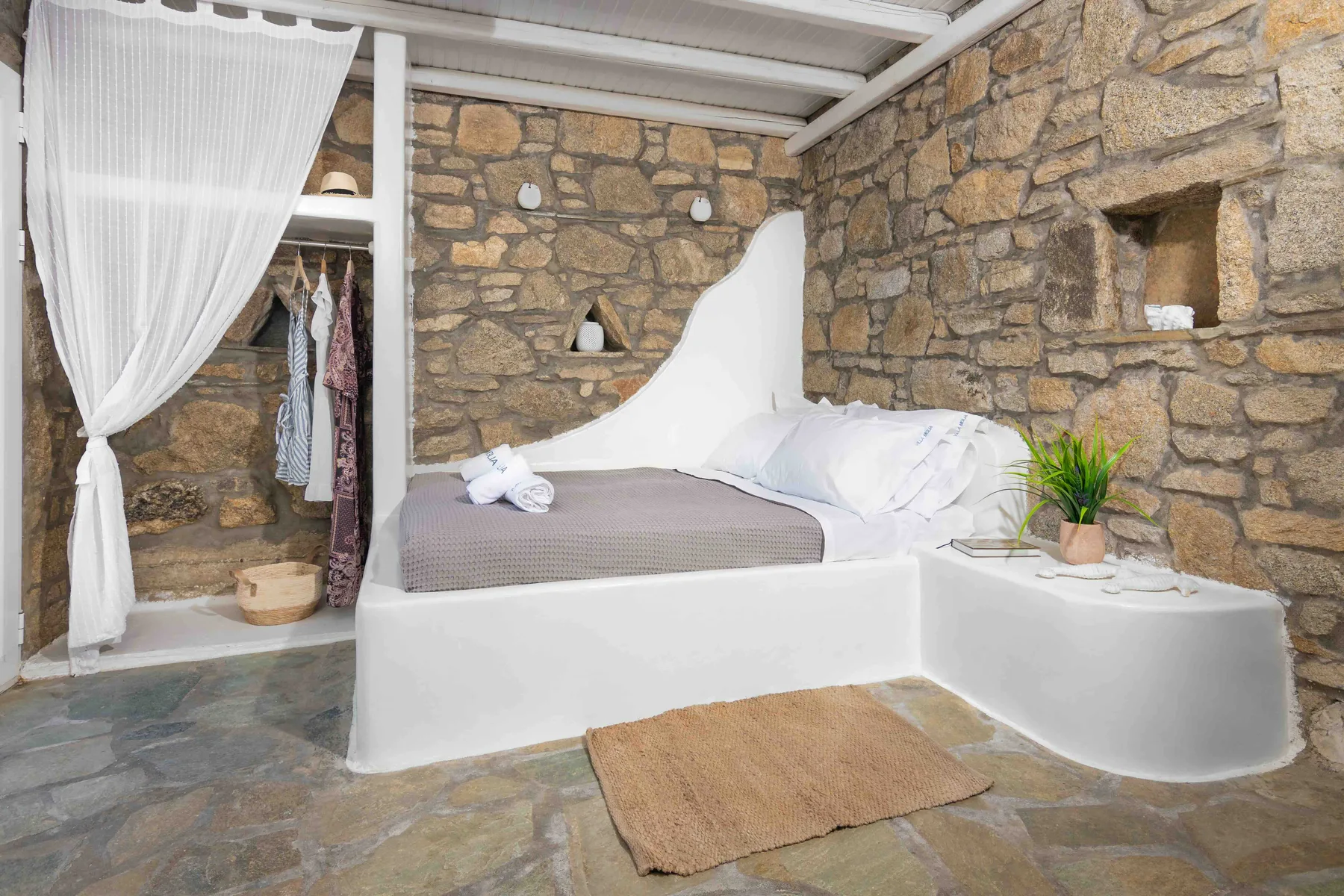 A bedroom with a built-in bed against stone walls and a curtained wardrobe.