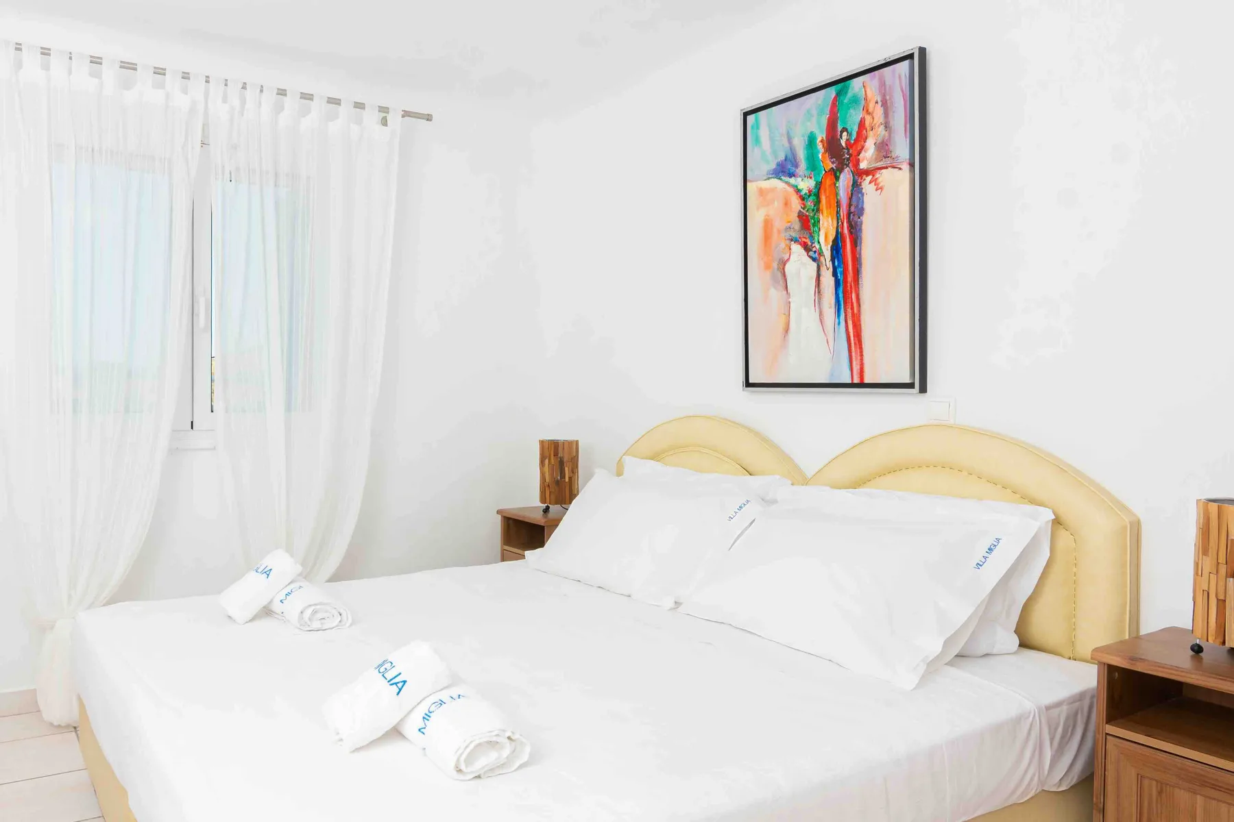A bright bedroom with a neatly made bed and colorful artwork above it.