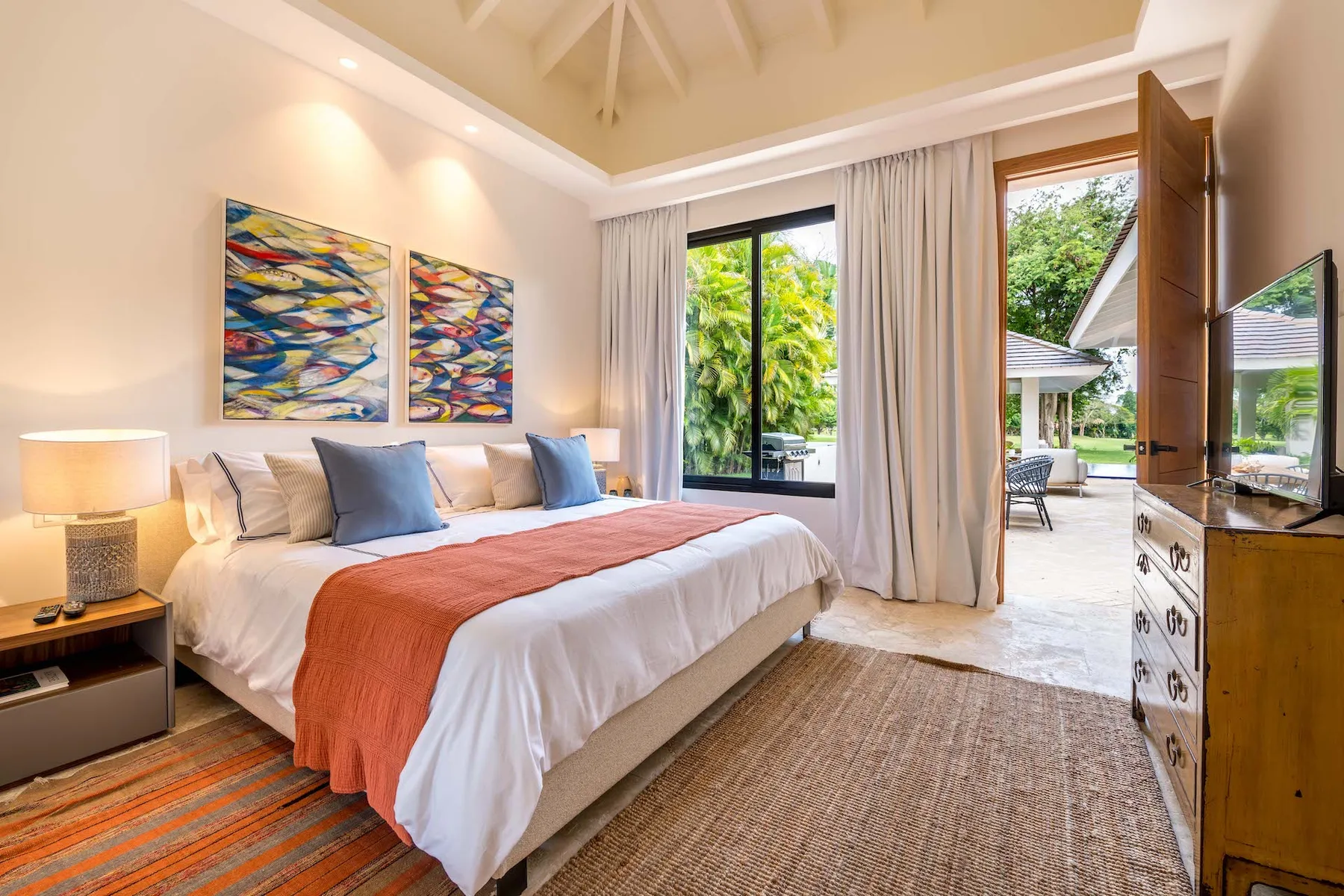 Un dormitorio con una cama grande, arte colorido en la pared y una puerta abierta al patio.