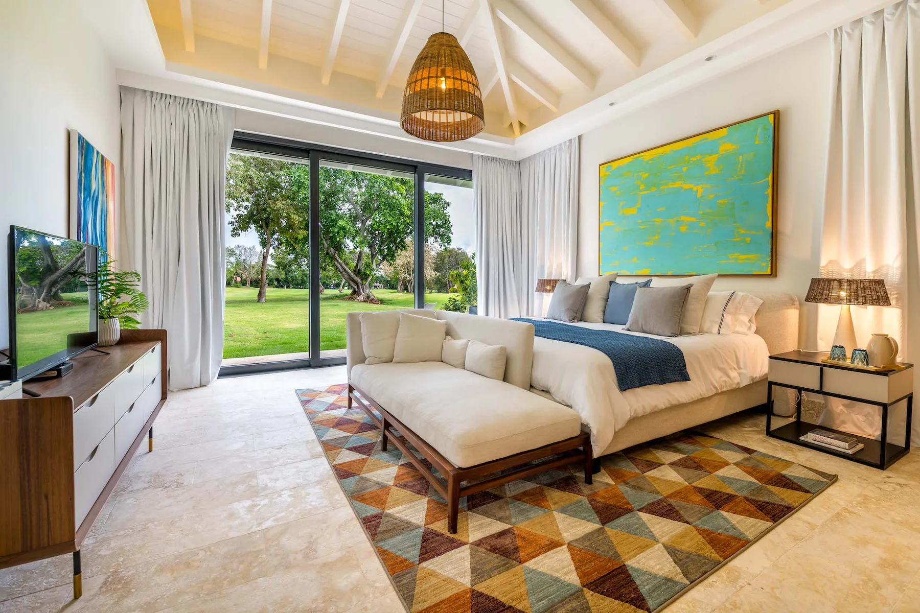 Un dormitorio luminoso con una cama grande, una alfombra colorida y puertas de vidrio hacia el jardín.