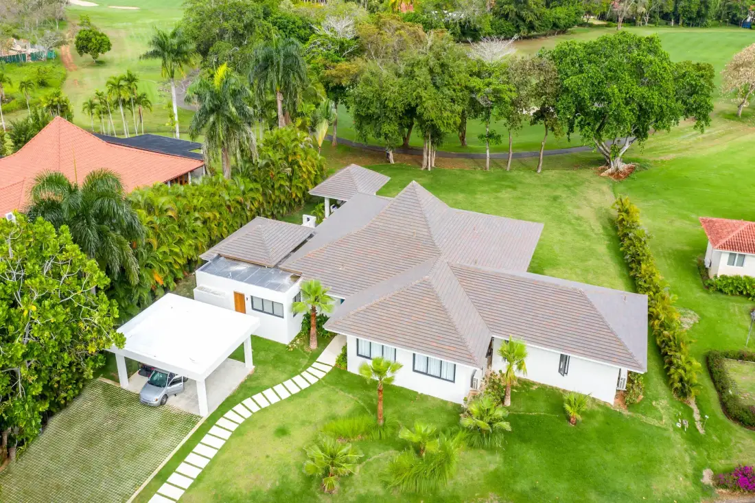 Vista aérea de una casa con techo de tejas, rodeada de césped y árboles verdes.