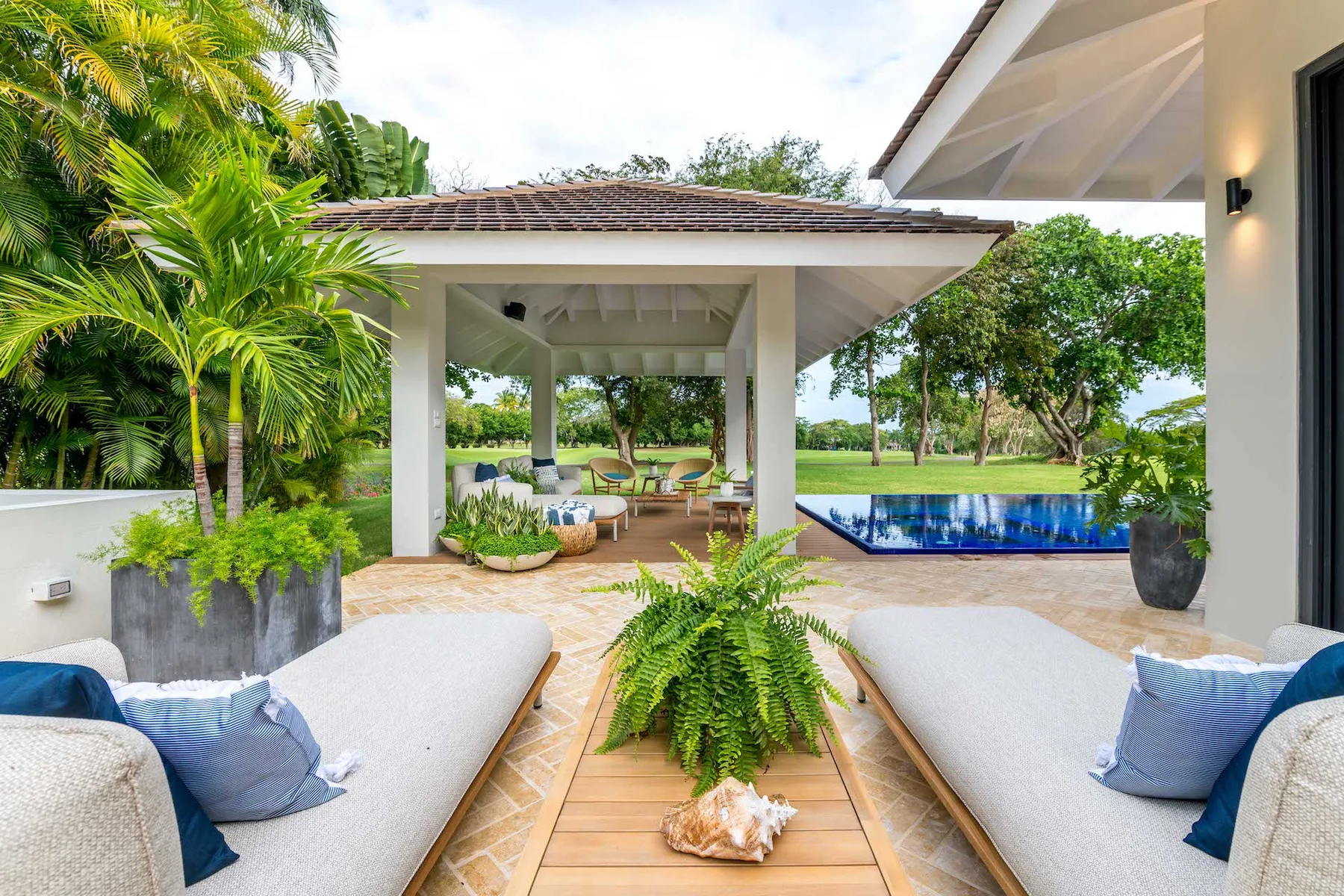 Una zona de estar al aire libre da a un patio cubierto y una piscina azul.