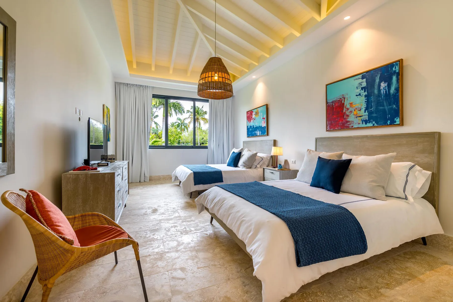 Un dormitorio luminoso con dos camas, ropa de cama azul y ventanas grandes.