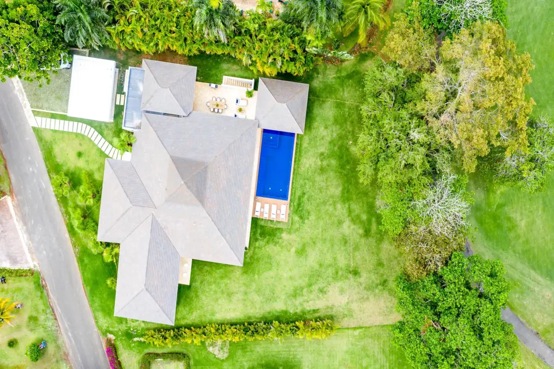 Vista aérea de una casa y una piscina azul rodeadas de césped verde.