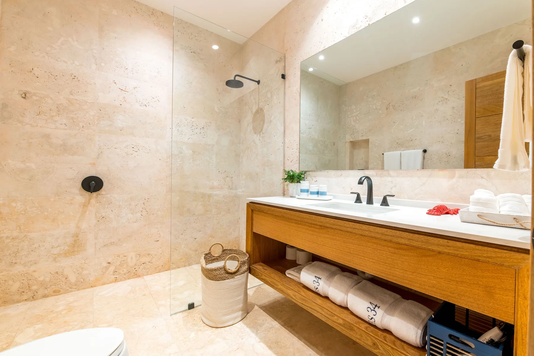 Un baño luminoso con ducha a ras de suelo y un tocador de madera bajo un espejo grande.